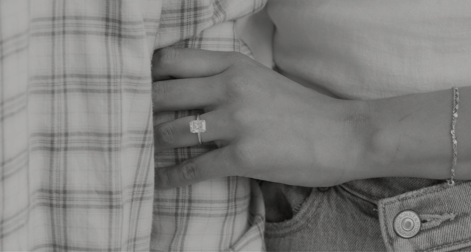 A person wearing a white shirt and blue jeans rests their hand on blue plaid fabric. They have a gold bracelet and a gol