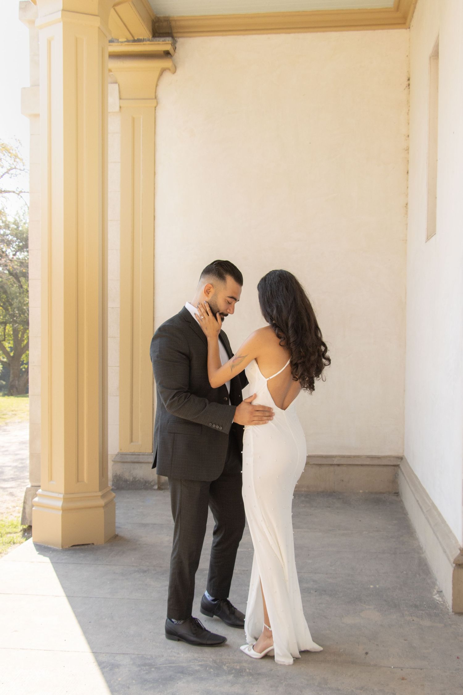 A couple slow dancing under a beige archway. The woman is in a white dress and the man is in a dark suit.