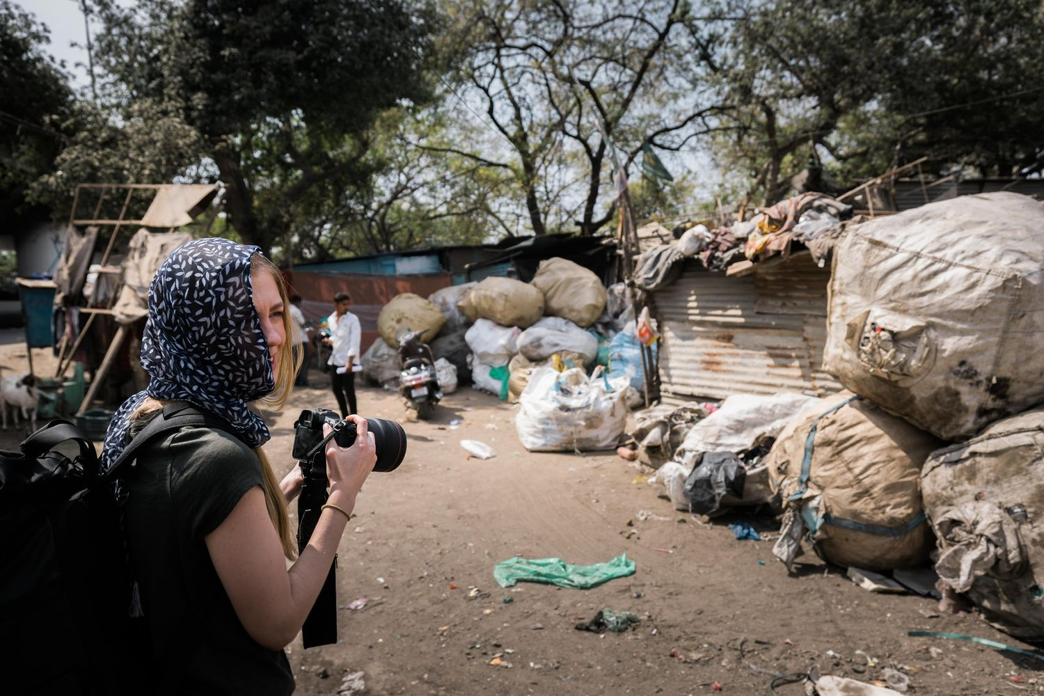 Photographer documenting piles of sorted recyclable materials and waste at an outdoor collection site.