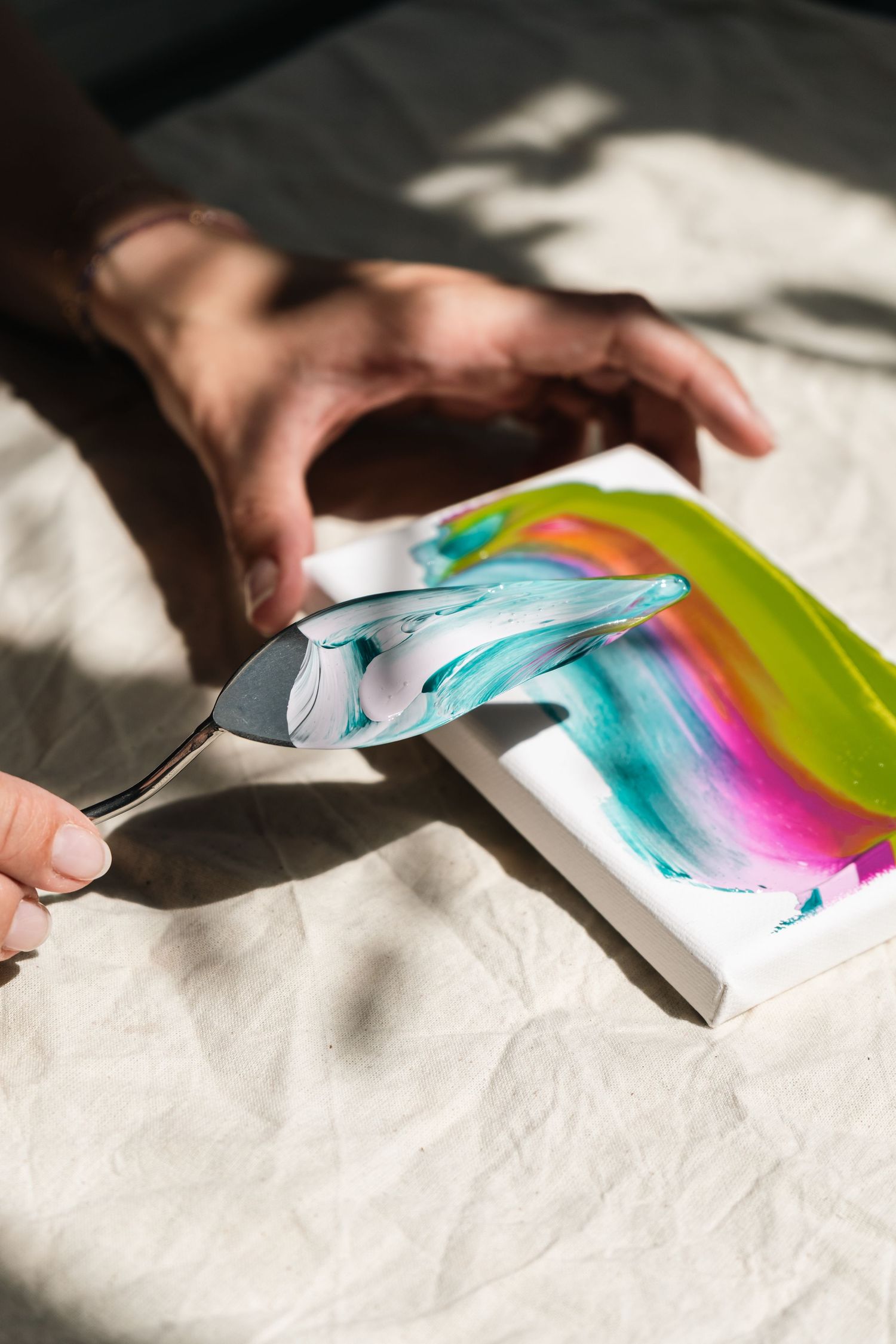 Artist using a palette knife to blend colorful acrylic paints on a small canvas in bright sunlight.