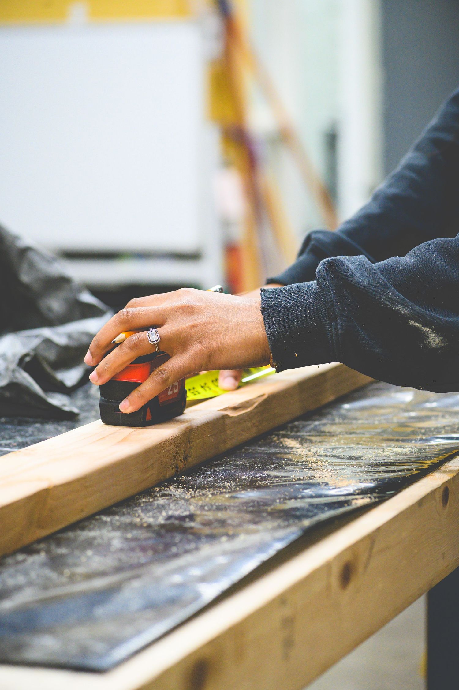Close-up view of hands using a measuring tape on a wooden plank at a workshop workbench.