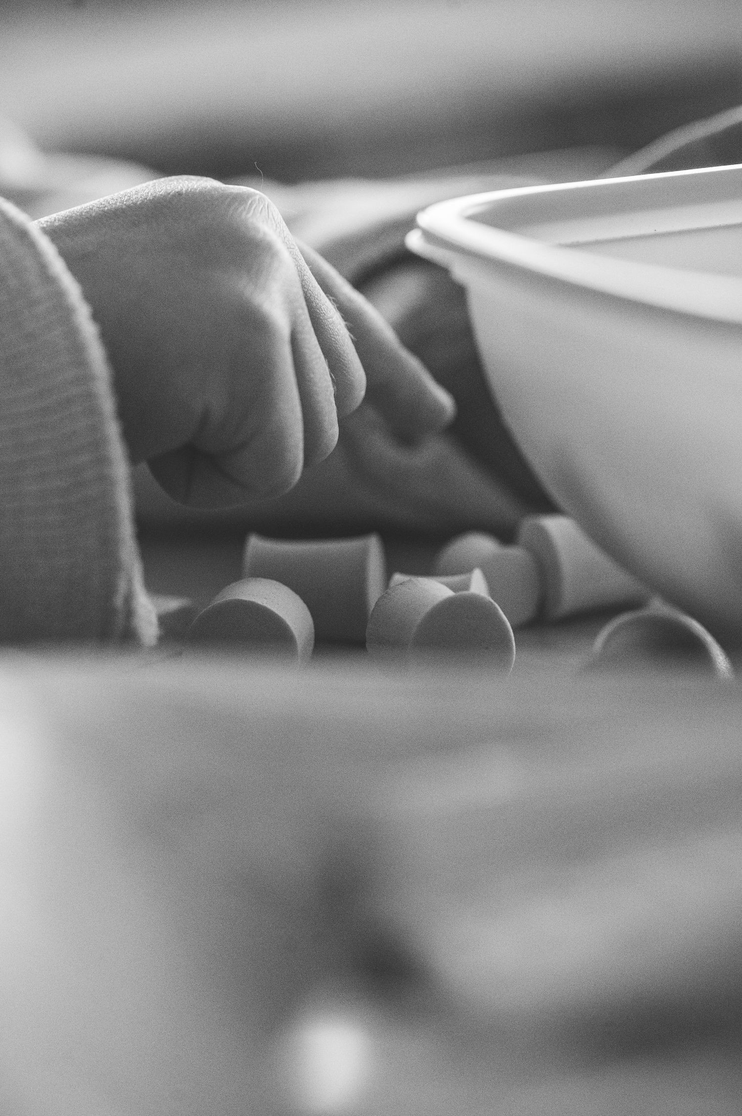 Close-up black and white photo of a baby hand resting near small cylindrical objects and a white bowl.