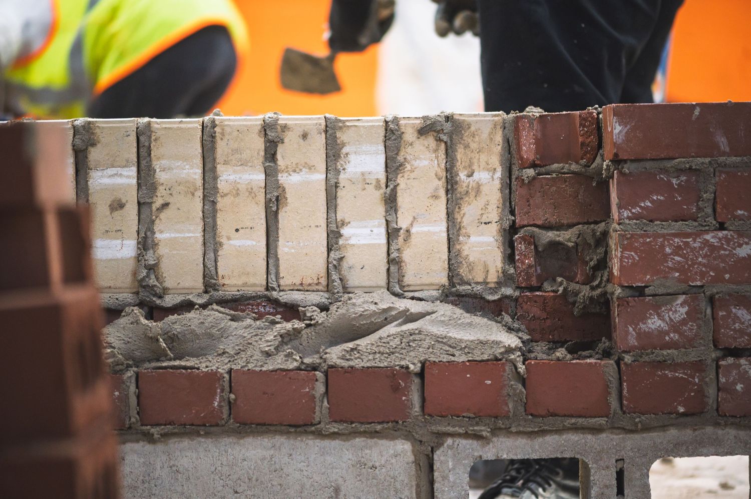 Bricklayer constructing a brick wall with mortar, showcasing professional masonry work at a construction site.