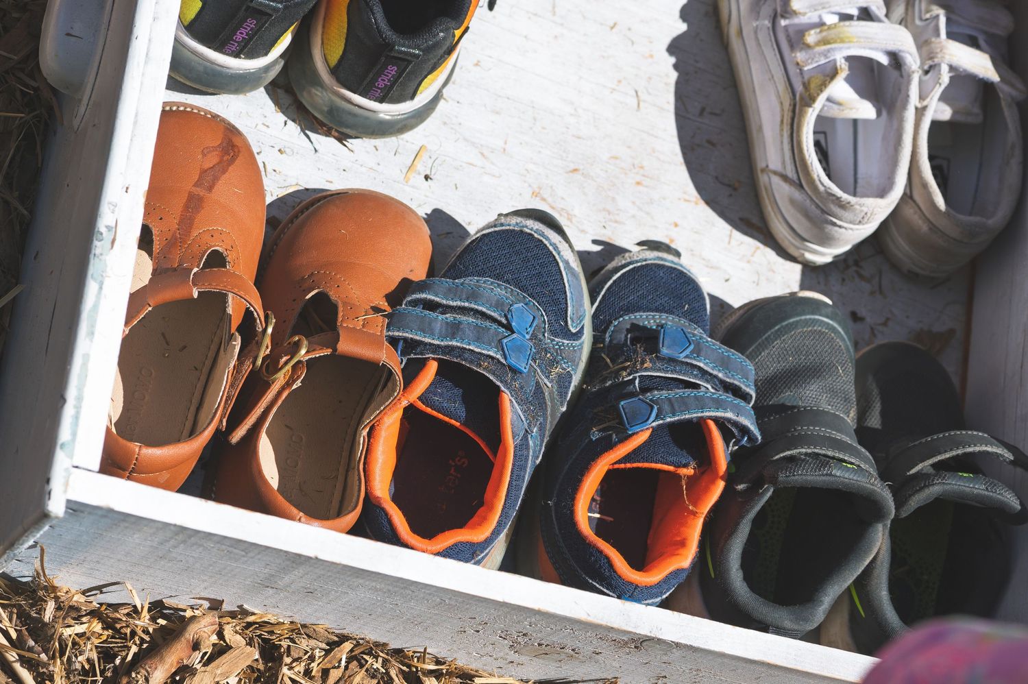 Multiple pairs of children's colorful shoes neatly arranged in an outdoor wooden shelf.