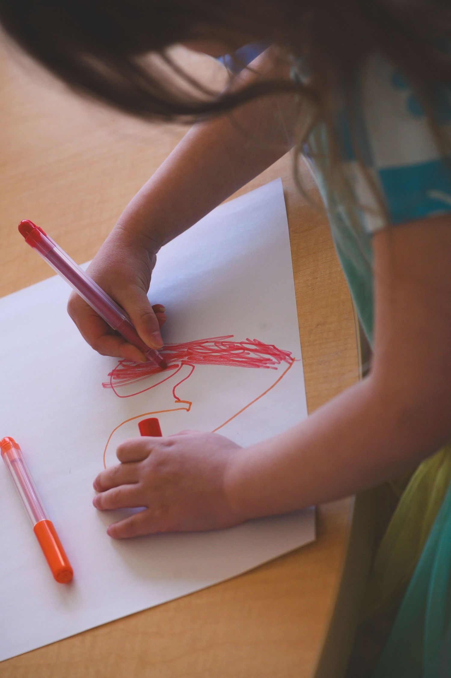 Young child drawing with red marker on white paper at a wooden table, showcasing early childhood creativity.