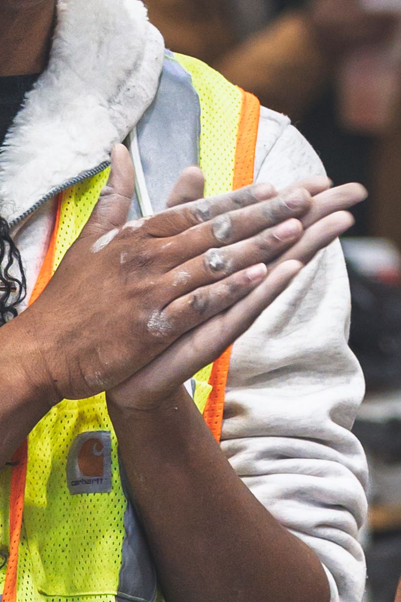 Construction worker in safety vest rubbing chalky white powder on hands outdoors.