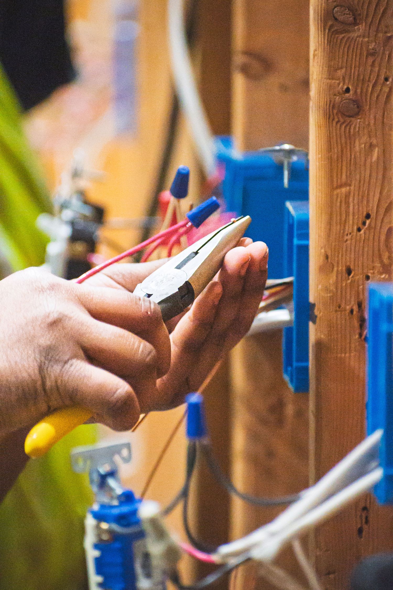 Electrician using pliers to wire blue electrical boxes mounted on wooden studs during home construction.