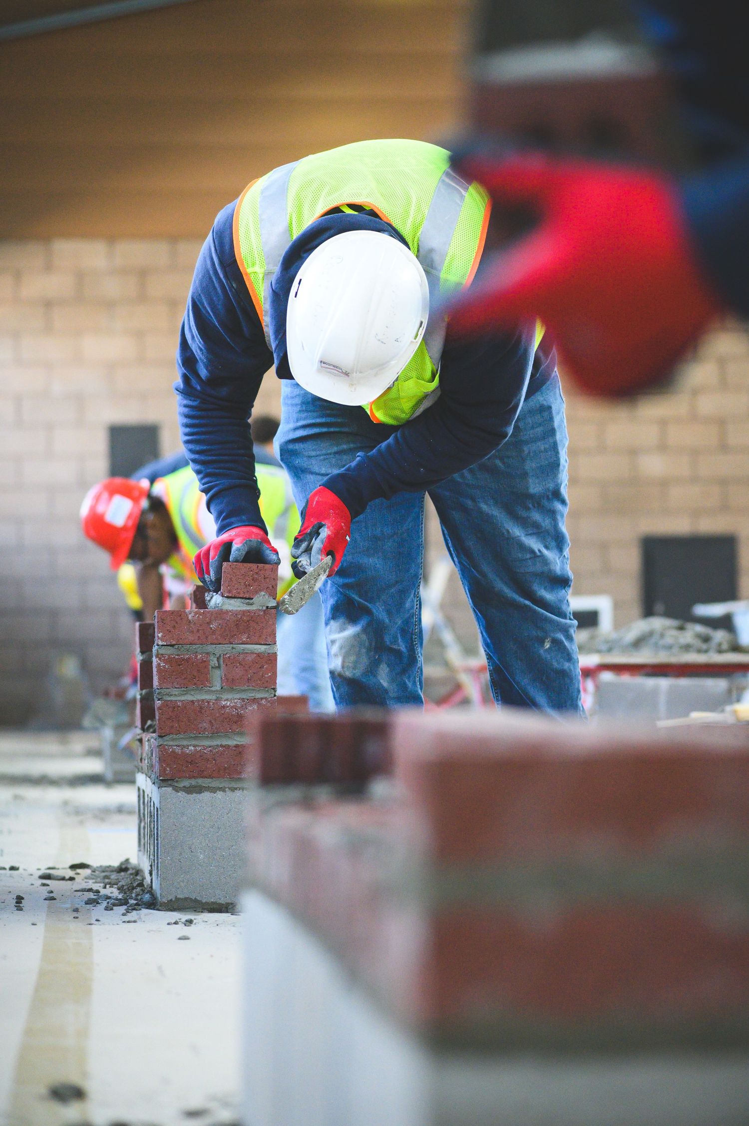 Construction worker in safety vest and hard hat laying red bricks on a building site.