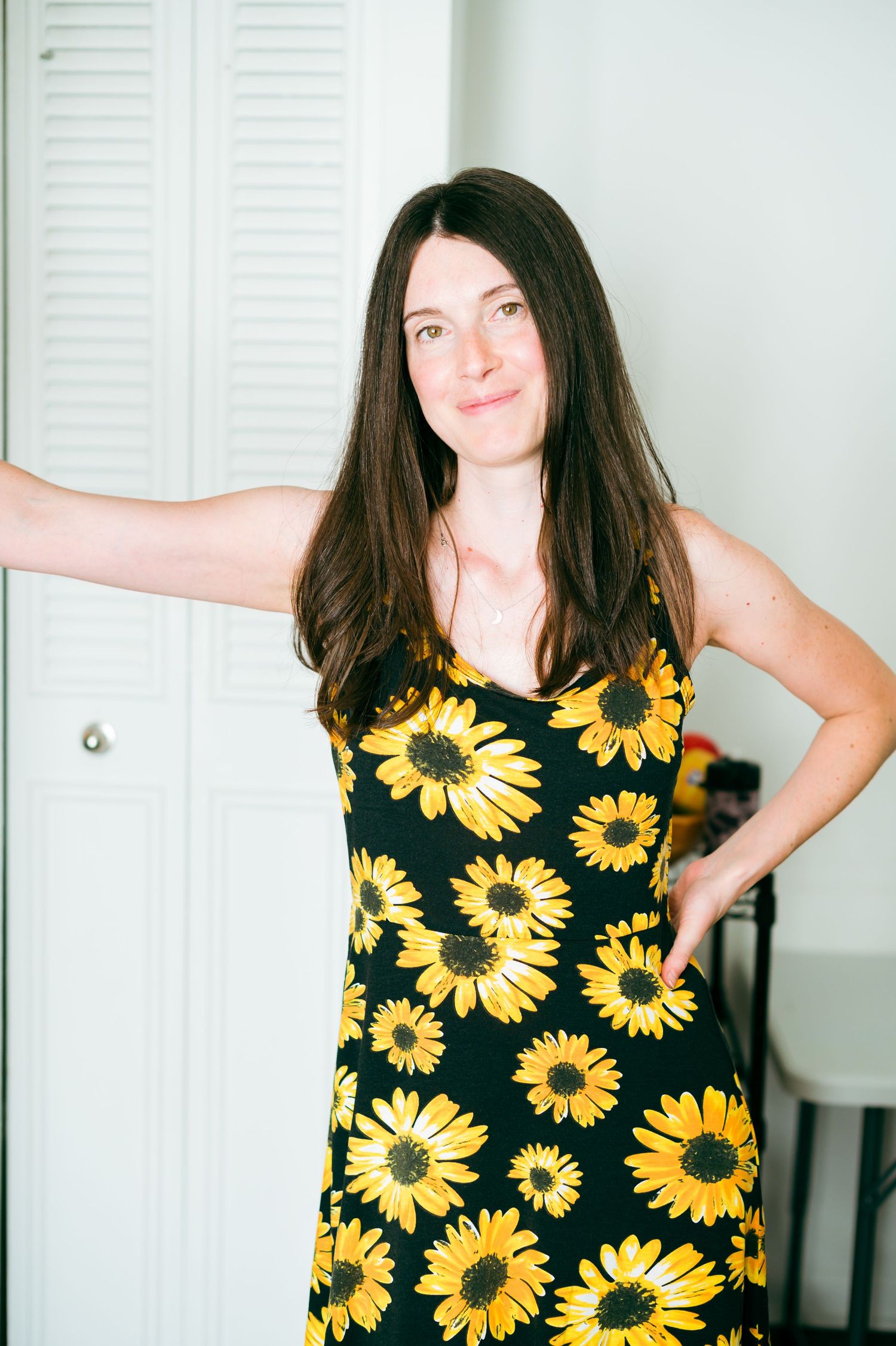 A series of poses in a sunflower print dress against a white door background.