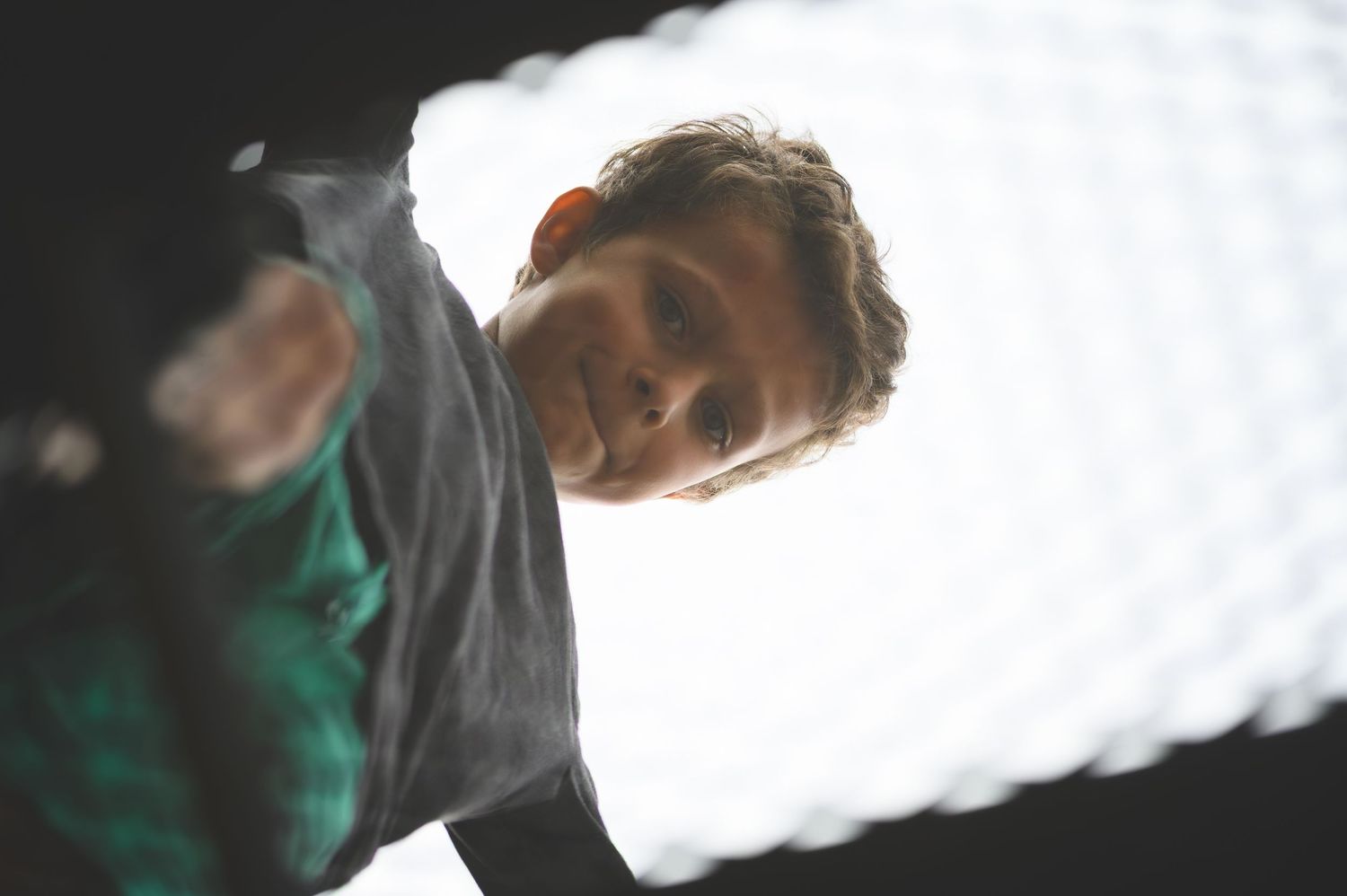 Figure bending down captured from below against a bright white background wearing a gray and green shirt.