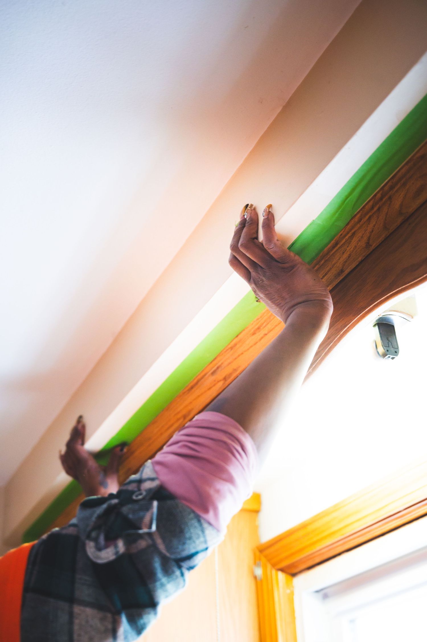 Hands reach up to work on installing wooden trim near a ceiling.