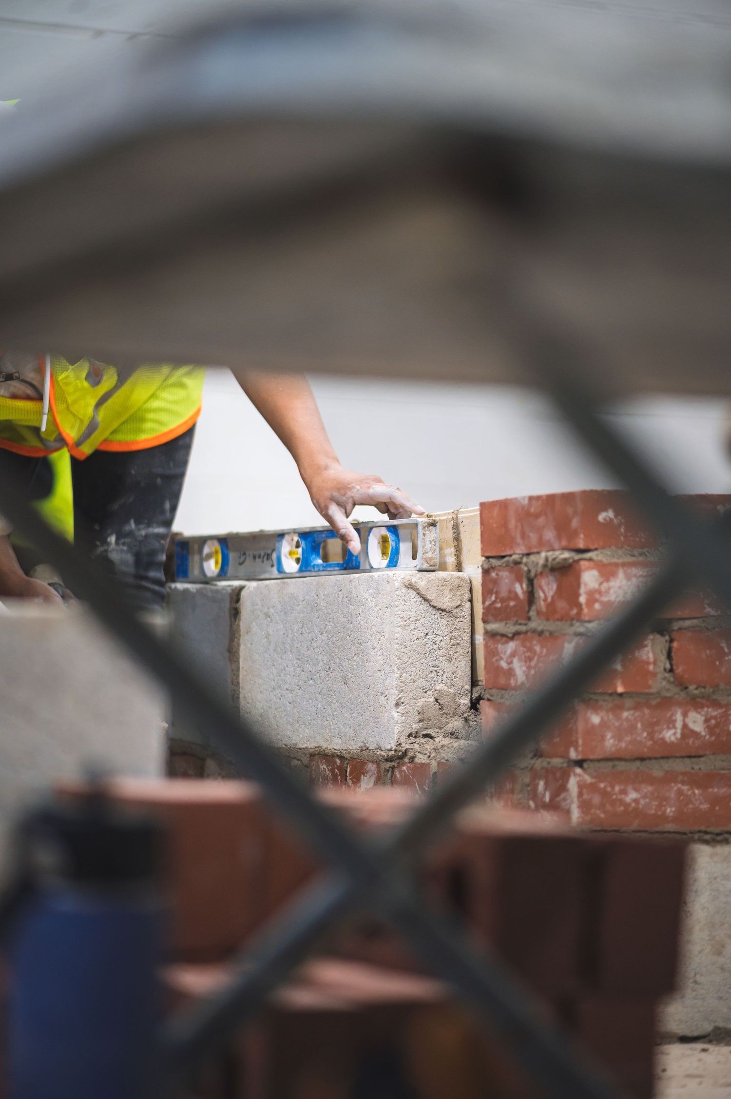 Construction worker in safety vest using a spirit level to check brick wall alignment at a building site.