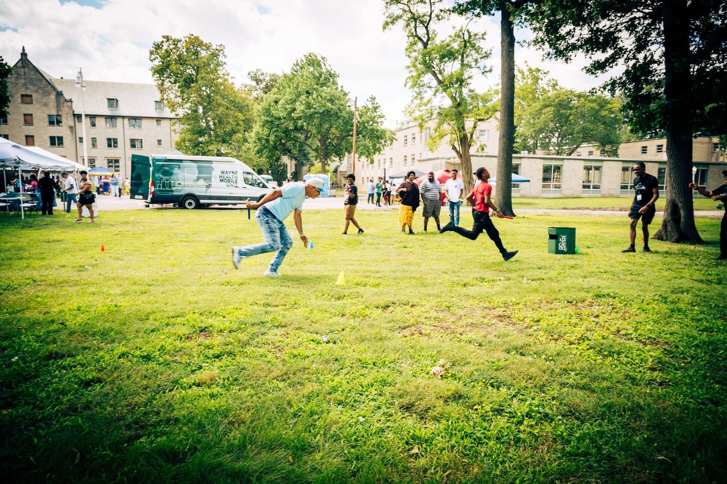 Children playing and running on a green lawn at an outdoor community event with food trucks and trees.