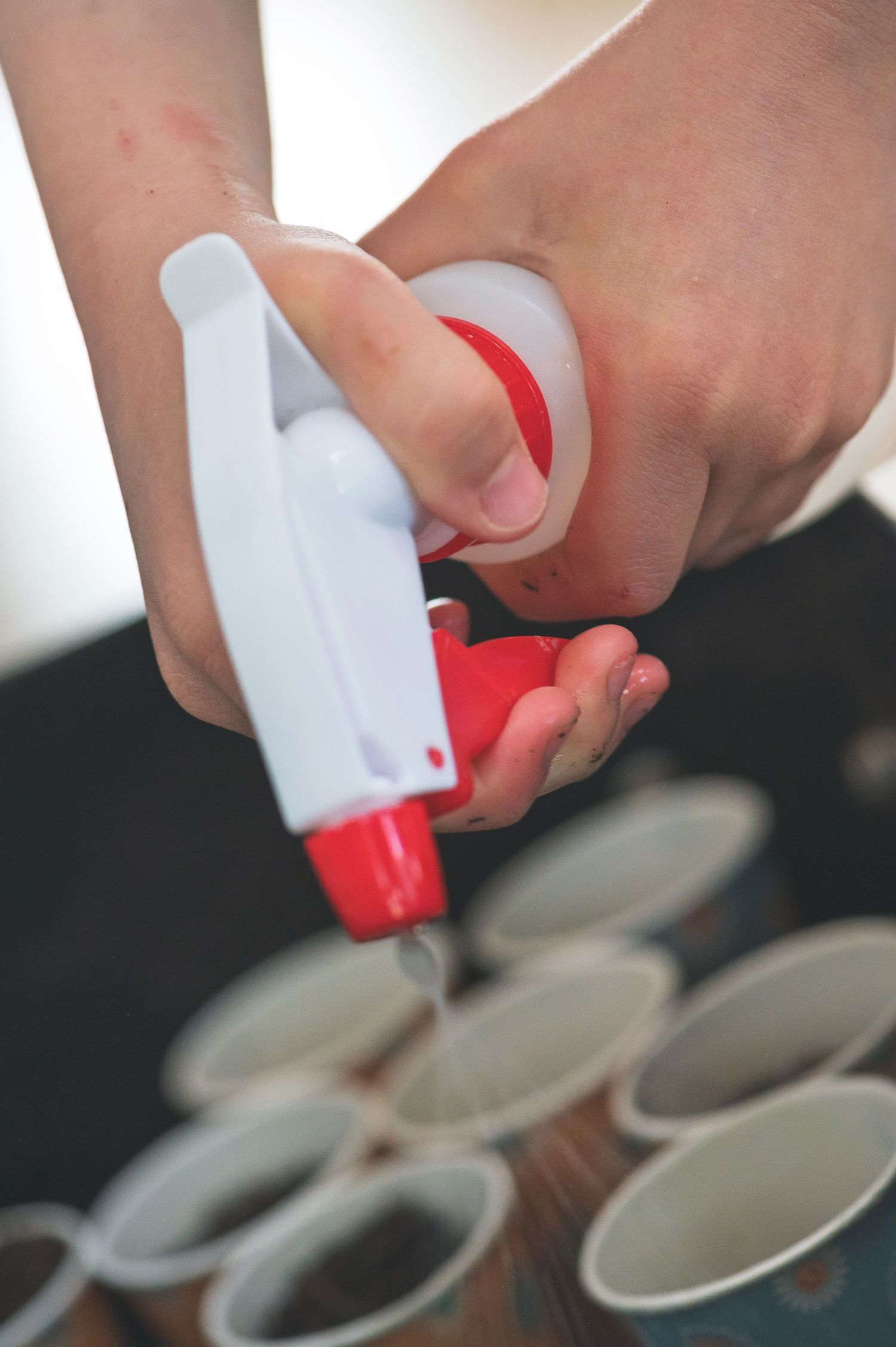 Person using a red and white glue gun over small white paper cups in a craft project.