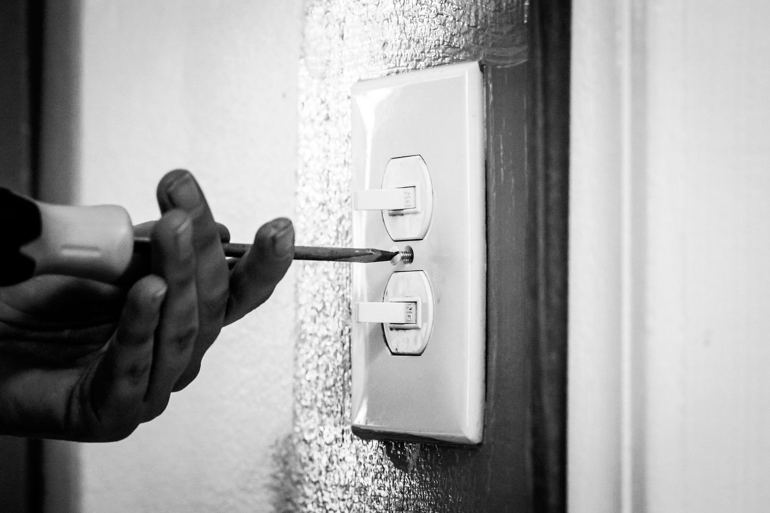 Close-up of a hand using a screwdriver to repair an electrical outlet switch.
