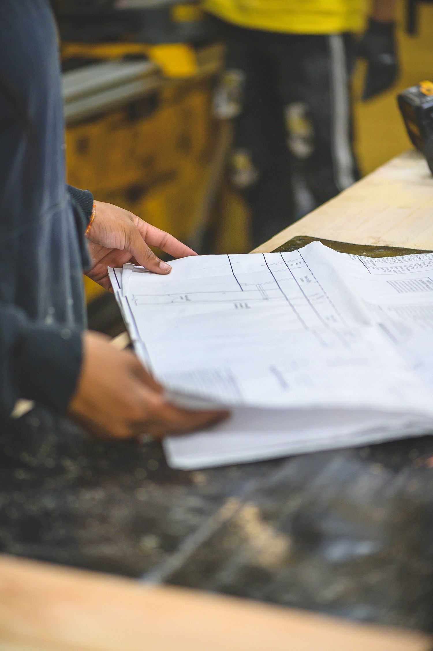 Person reviewing architectural or engineering blueprints and construction documents on a dark surface.