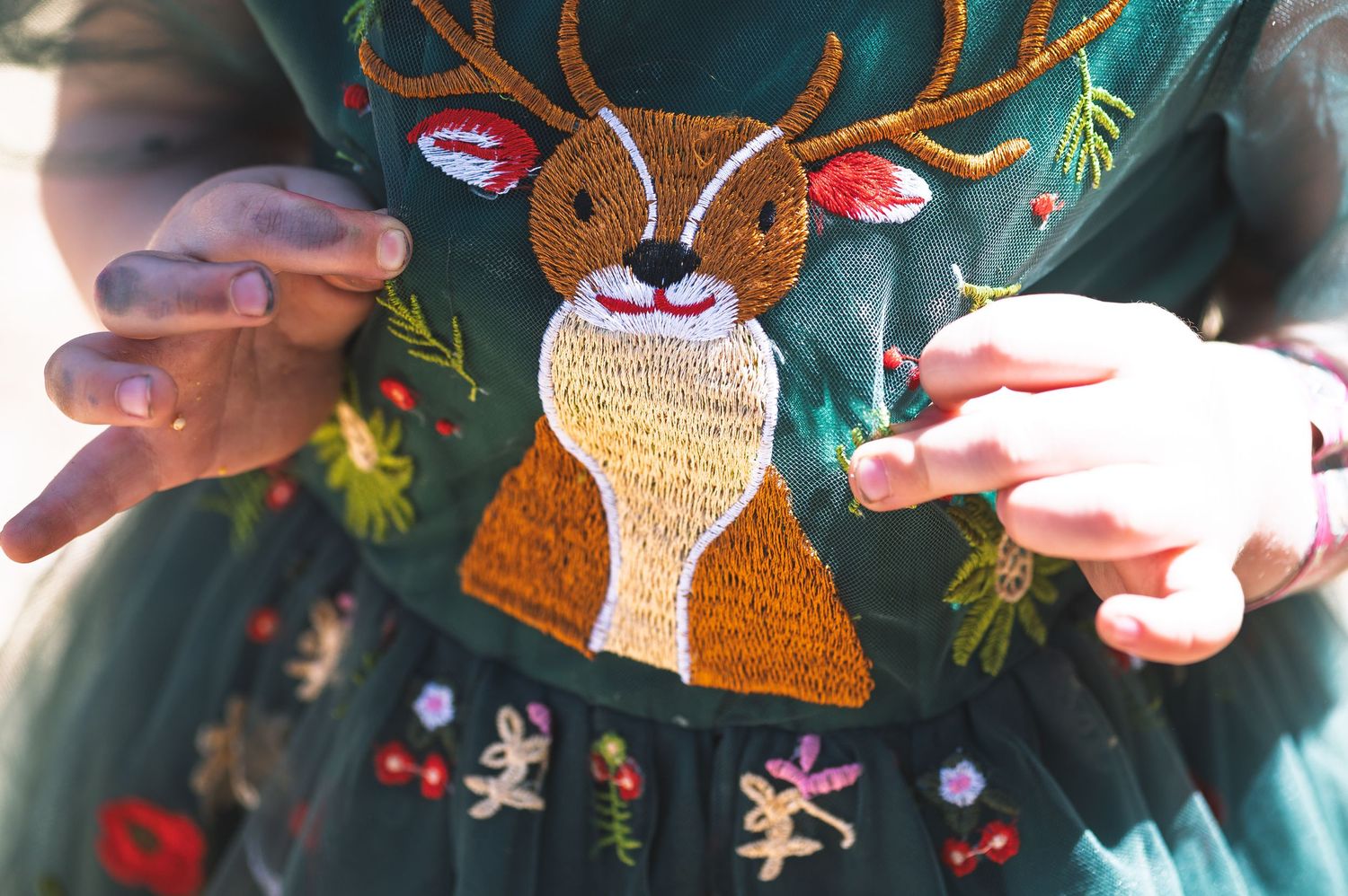 Close-up of a green embroidered dress featuring a detailed reindeer patch surrounded by festive holiday floral designs.