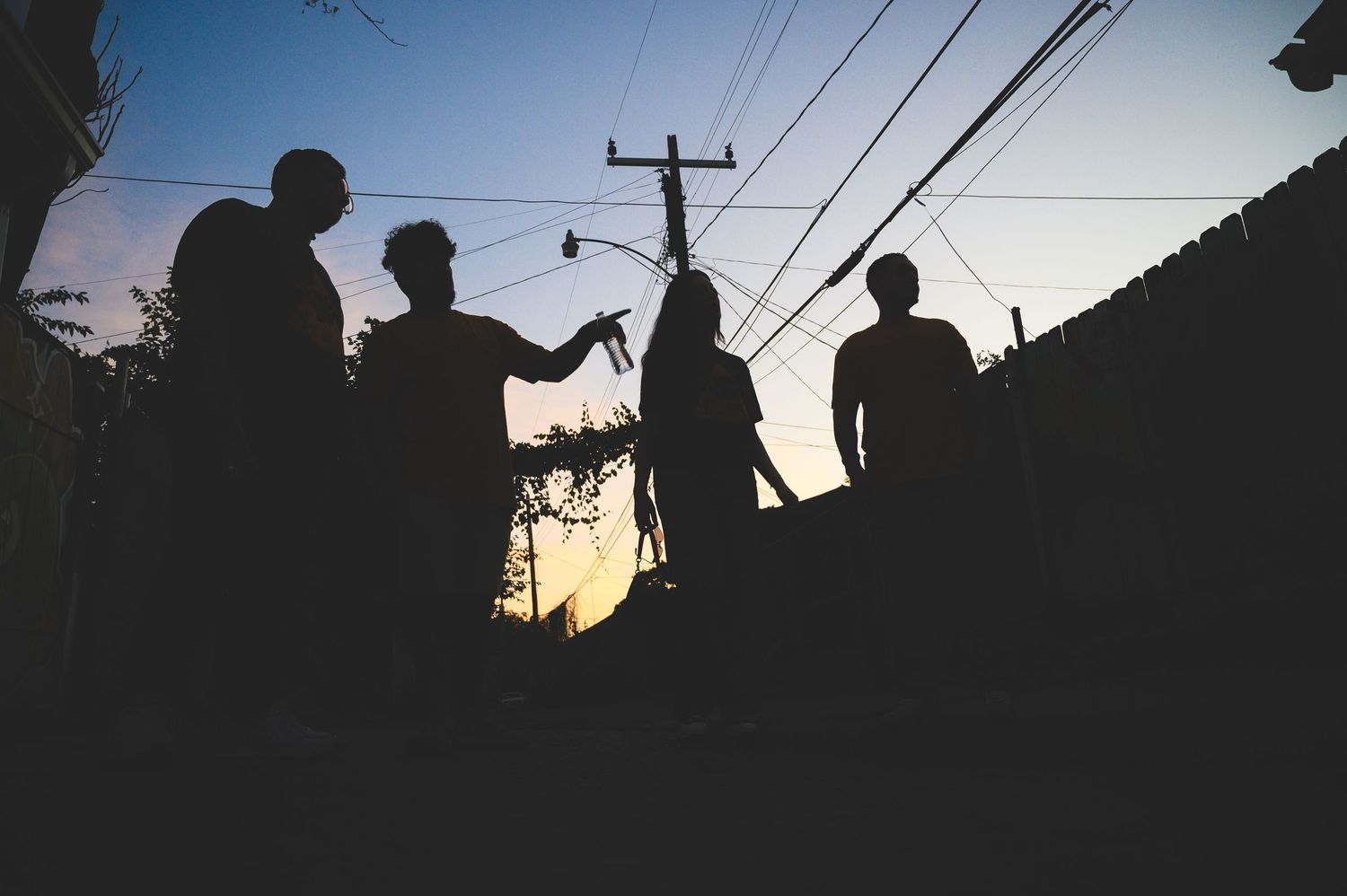 Silhouettes of people against a sunset sky with power lines and poles creating a dramatic urban landscape.