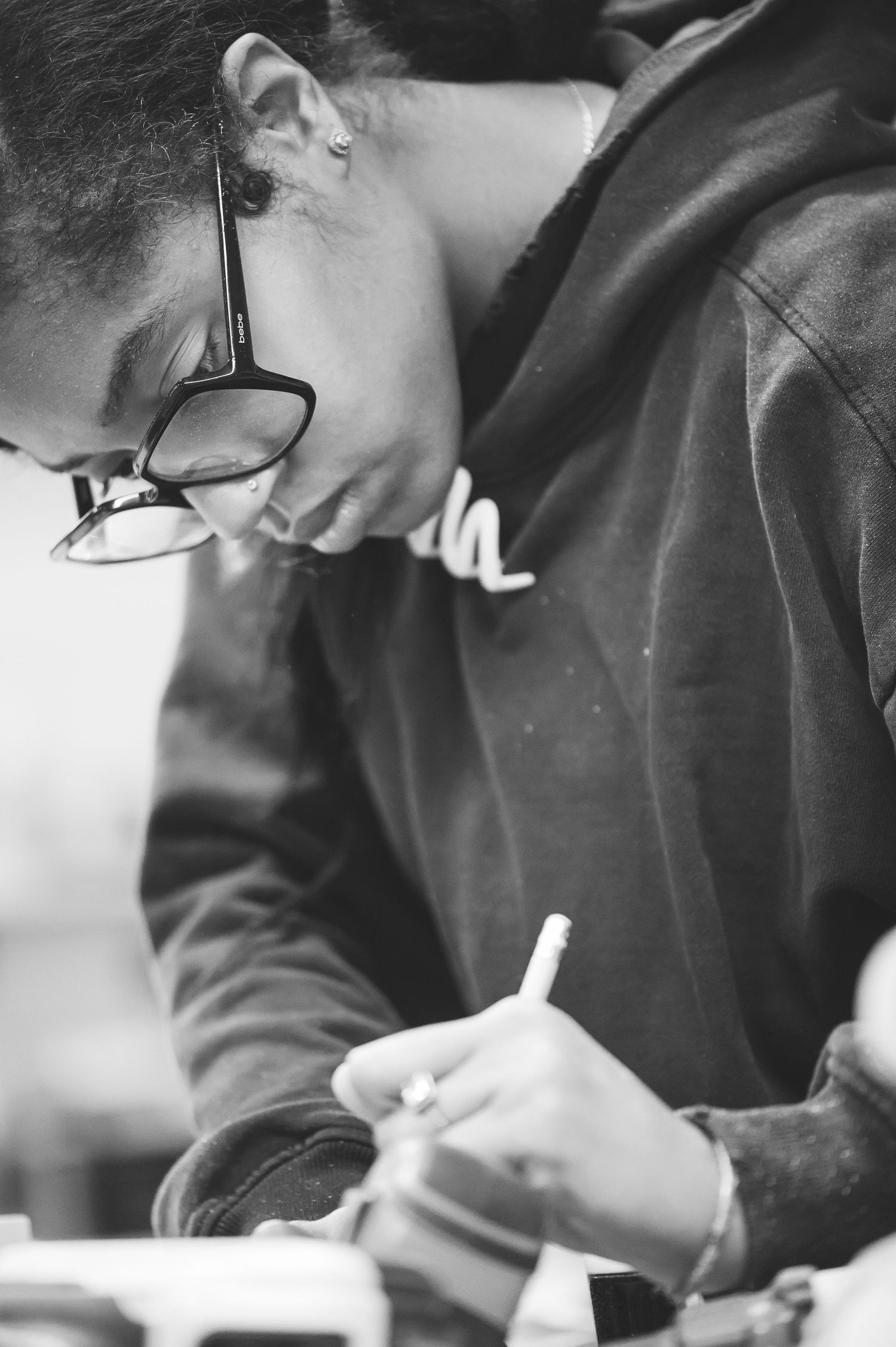 Black and white photograph of a student wearing glasses writing or studying at a desk in closeup profile view.
