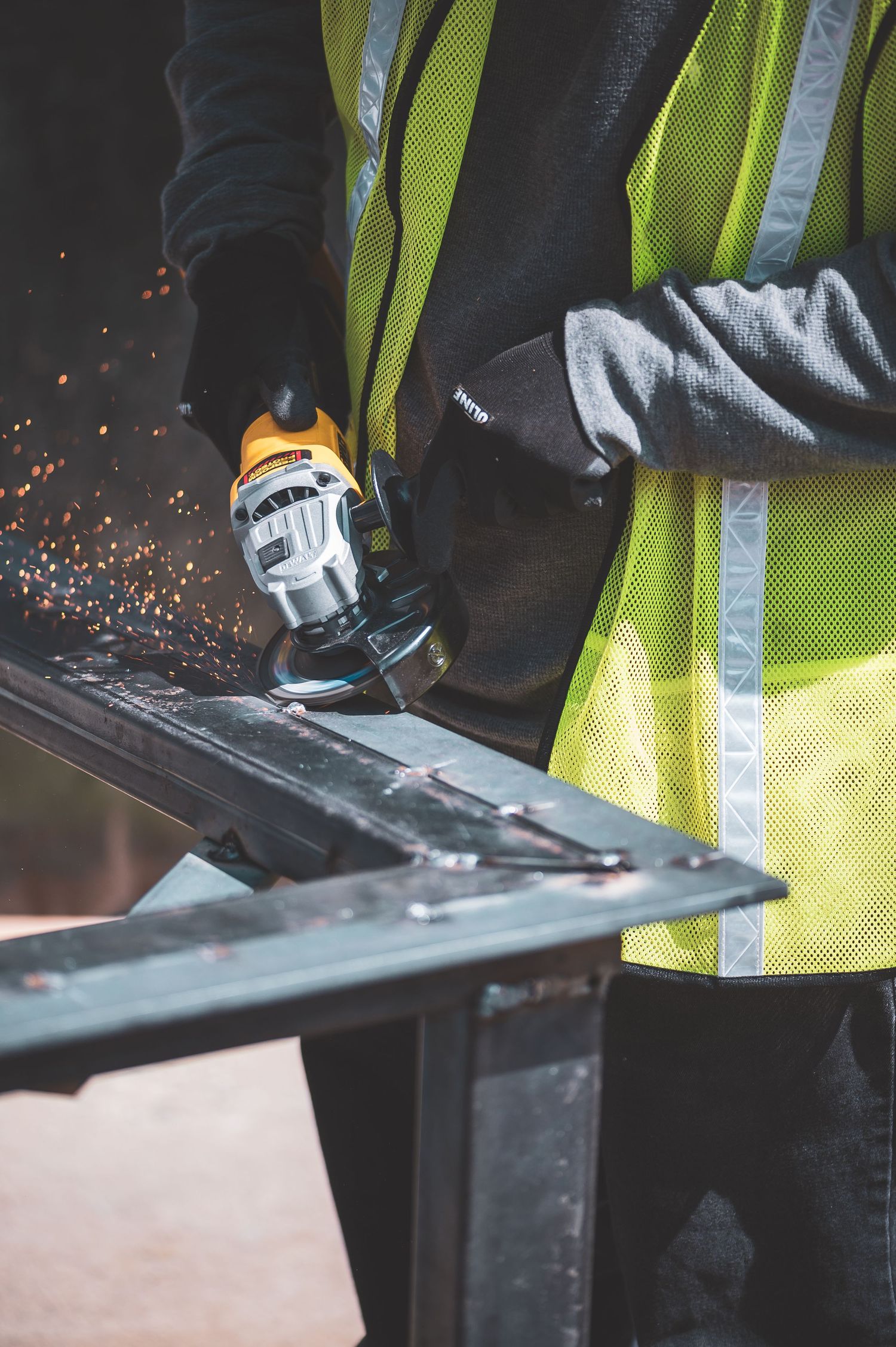 Worker in safety vest uses angle grinder on metal, sending sparks flying in a construction setting.
