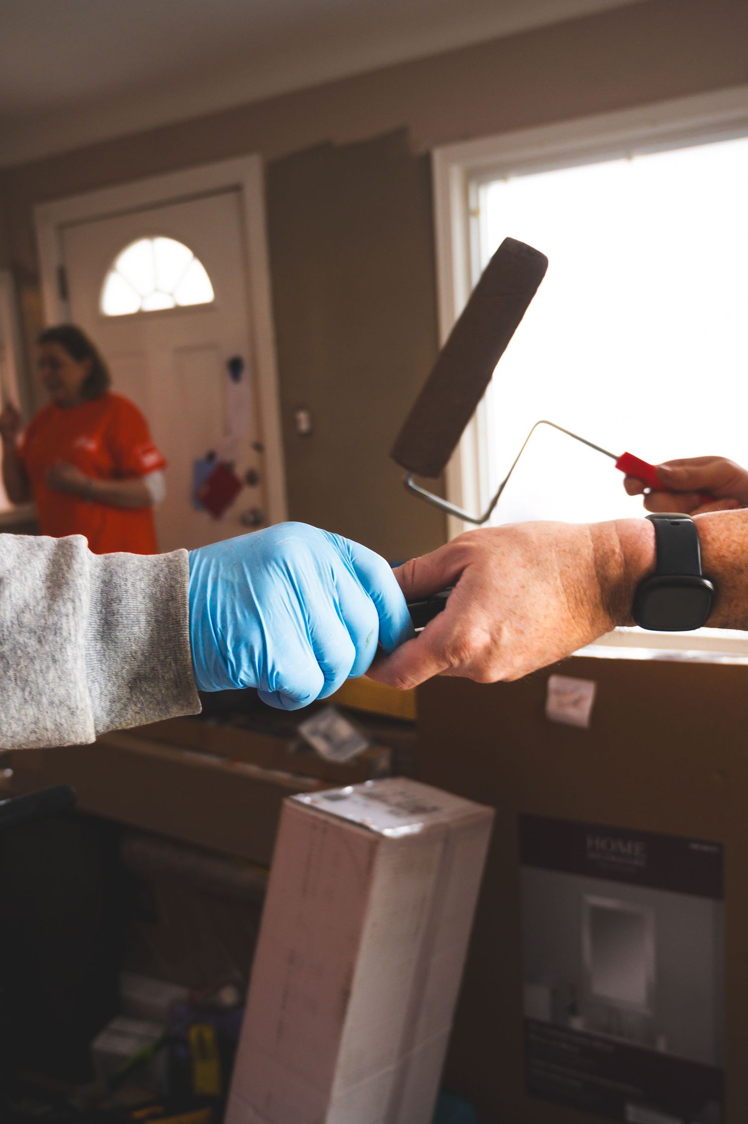 Hands wearing blue gloves holding paint roller during home improvement project.