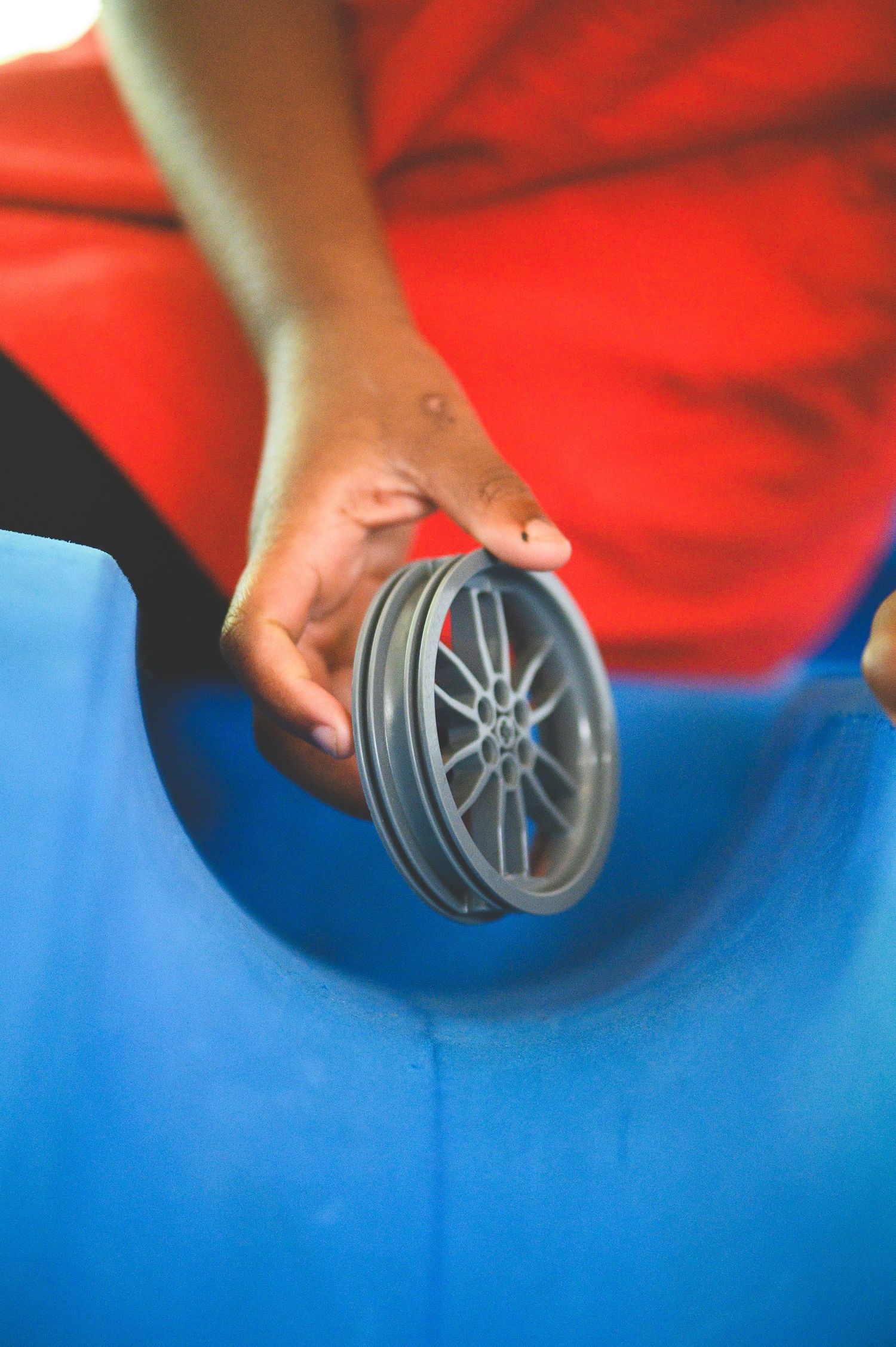 Hand holding a small gray alloy wheel model against blue and red fabric background.