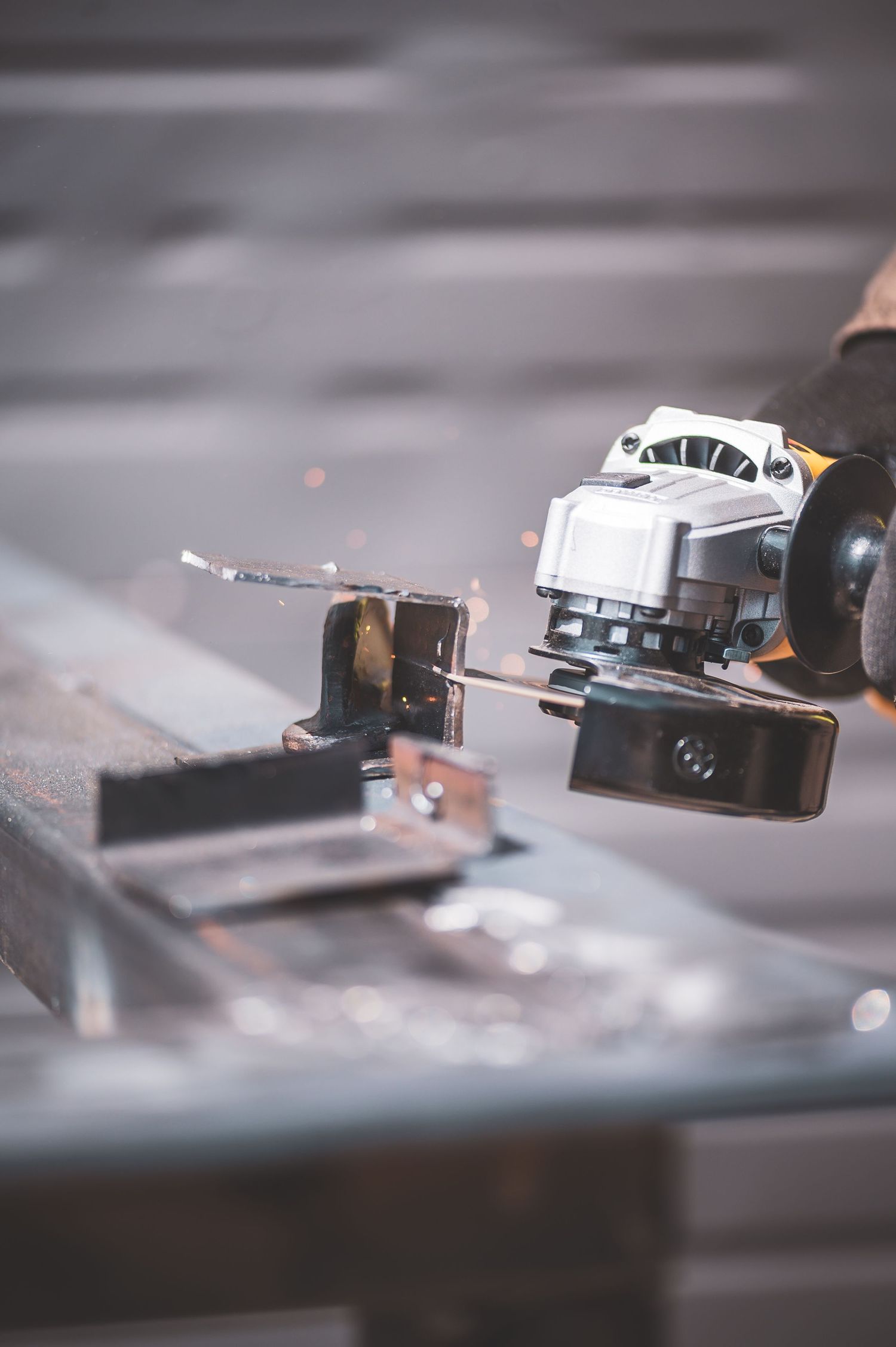 Worker using an angle grinder on metal with sparks flying in an industrial workshop setting.