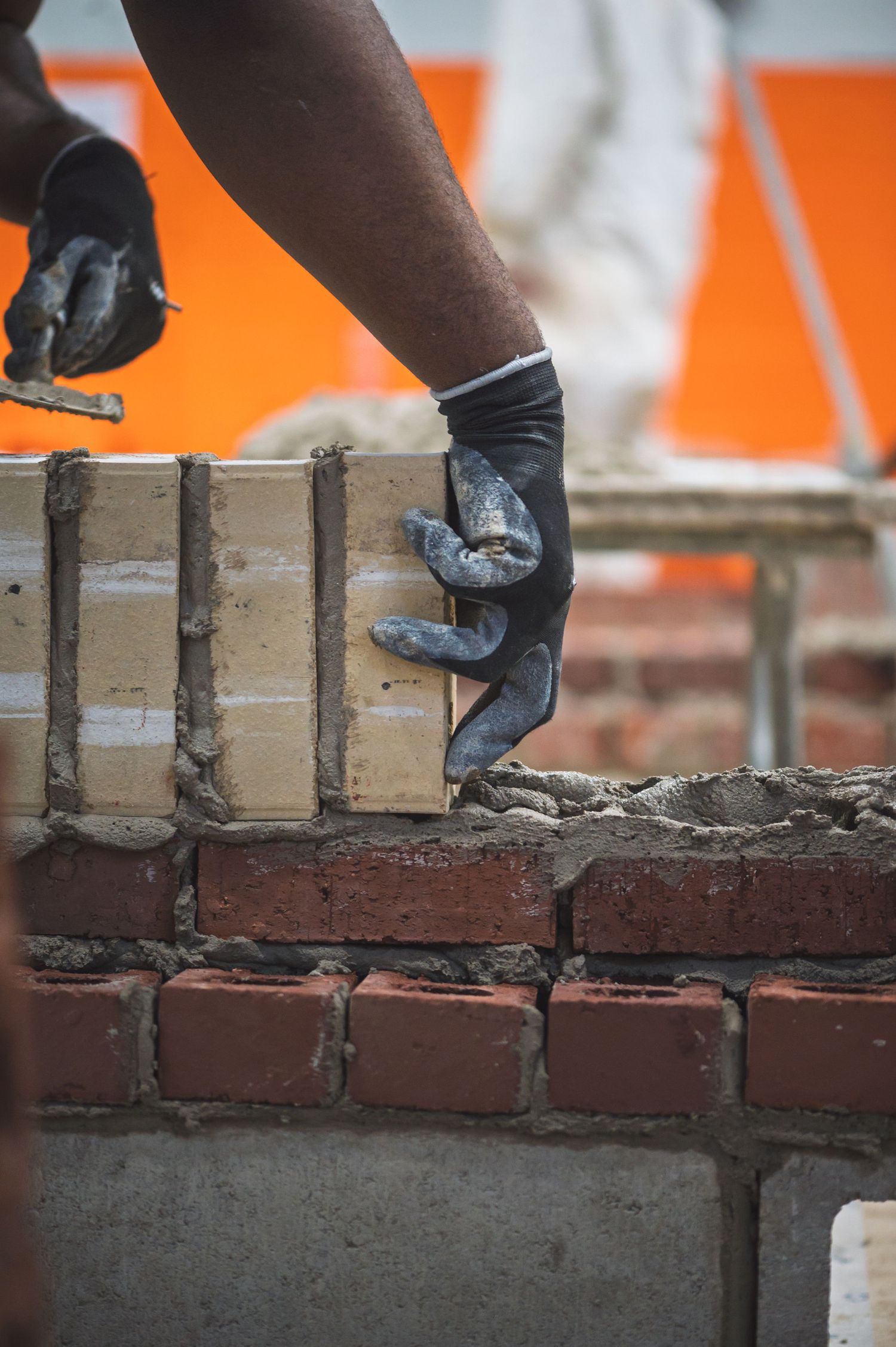A bricklayer wearing black gloves carefully lays bricks with mortar on a construction site.