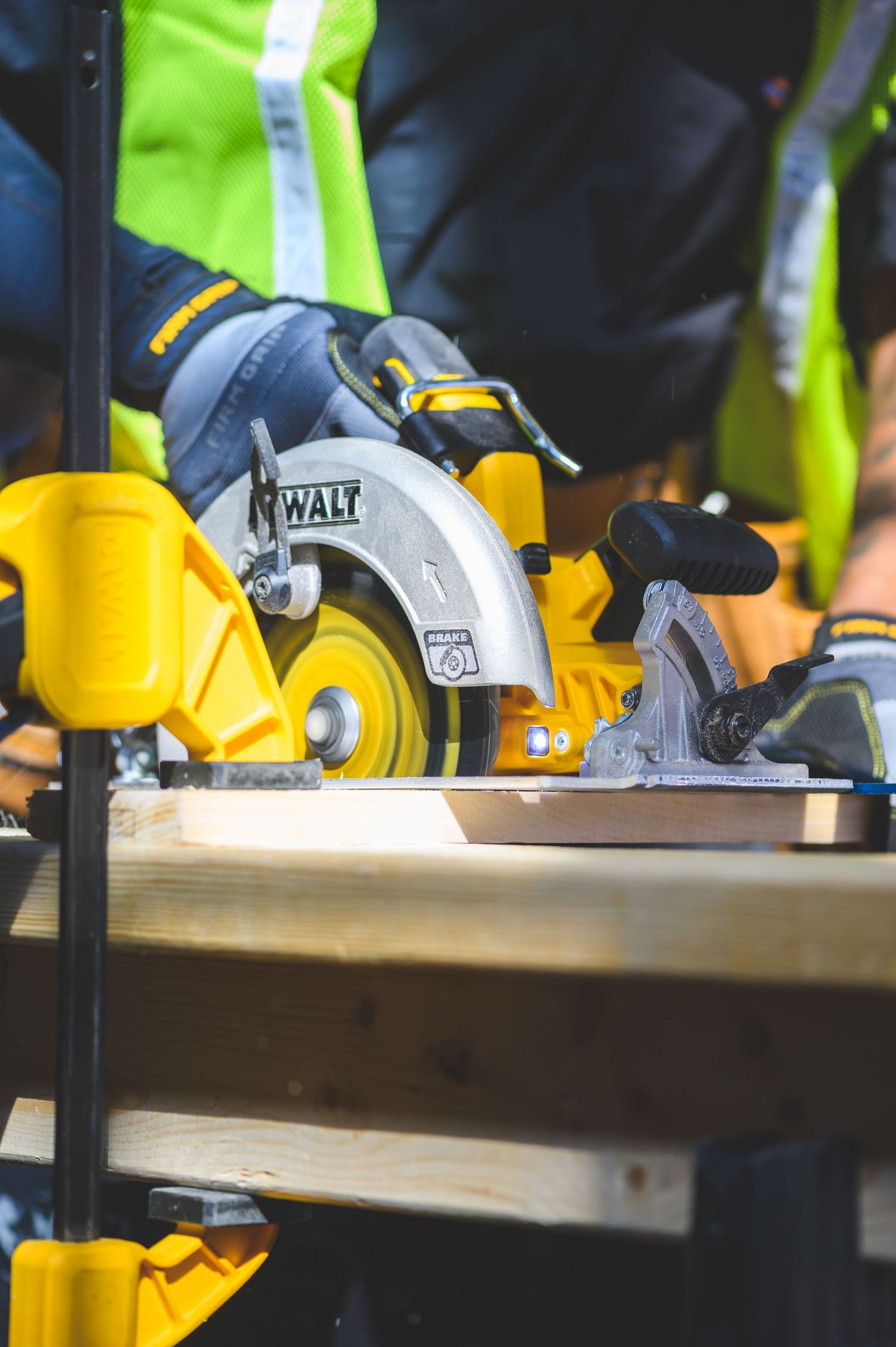 Worker in safety vest uses a DeWalt circular saw to cut lumber on a workbench at a construction site.