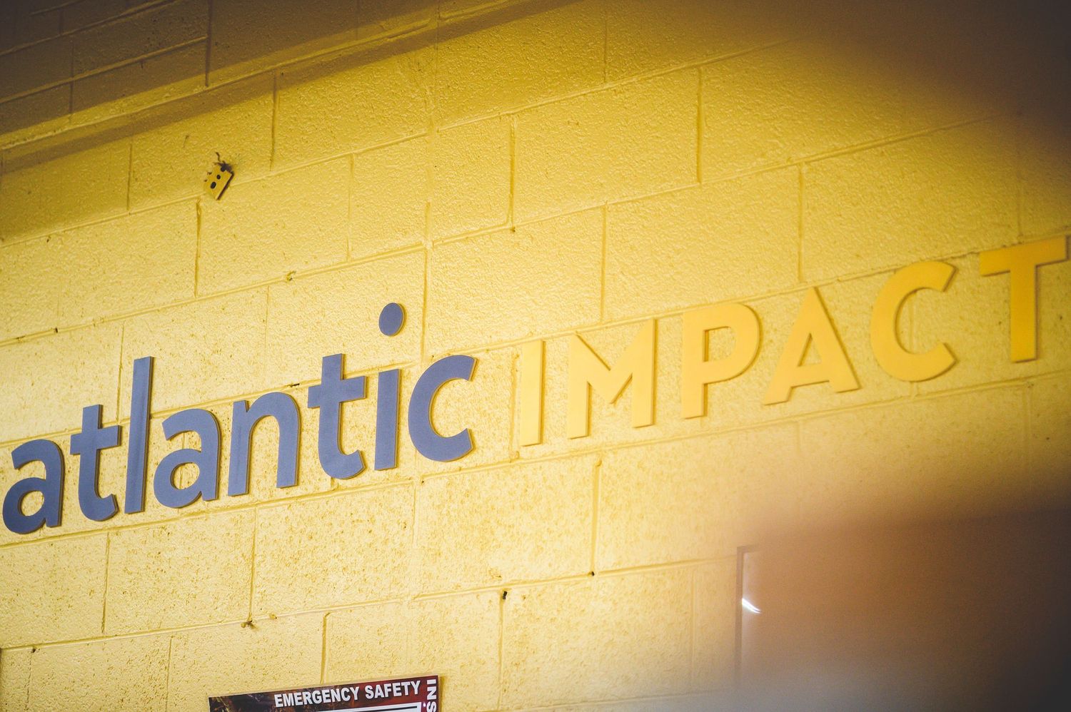 The text 'atlantic impact' appears in gray and yellow lettering on a white wall with dramatic lighting effects.