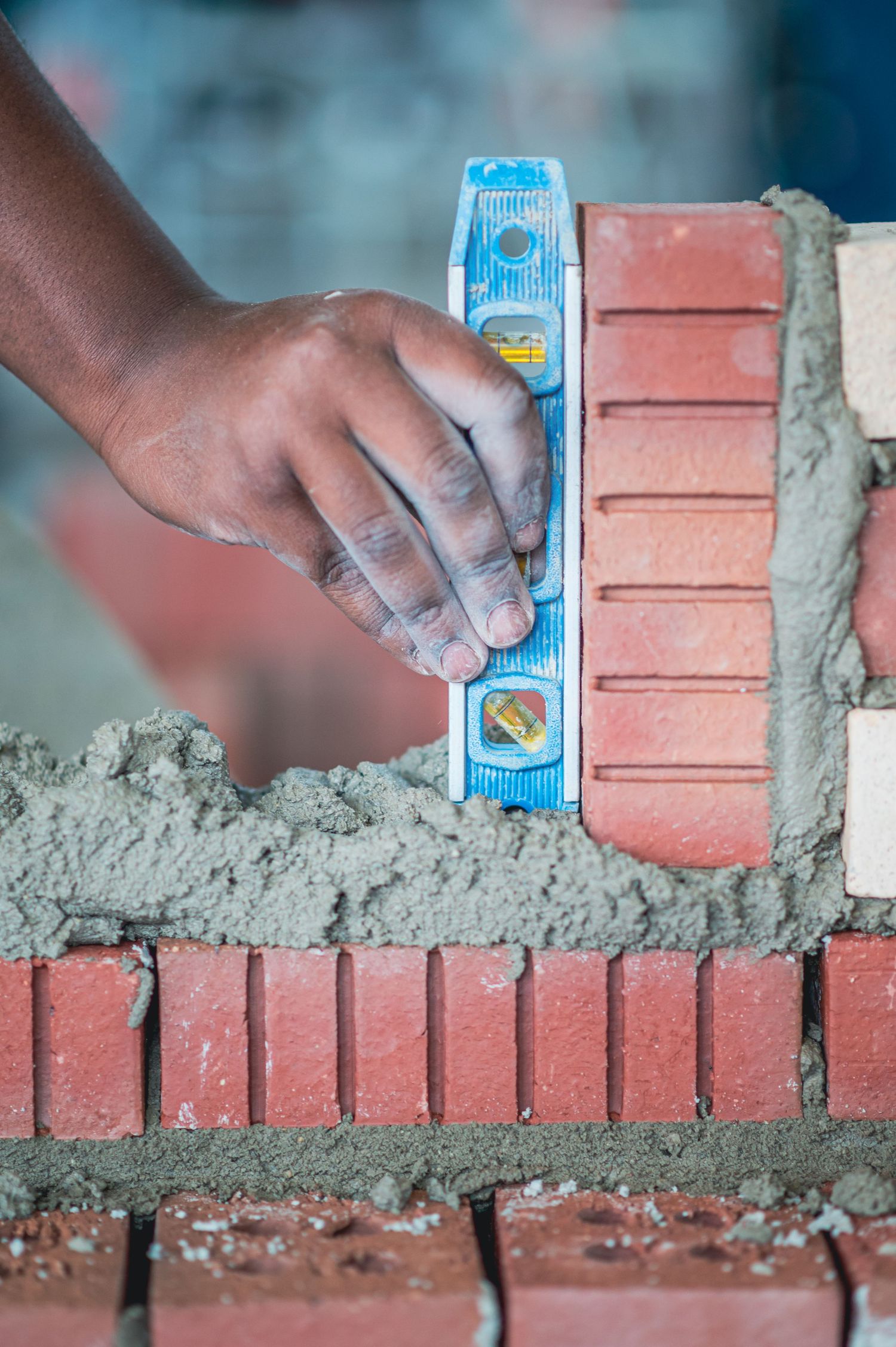 A bricklayer uses a spirit level to ensure accuracy while laying red bricks with fresh mortar on a construction site.