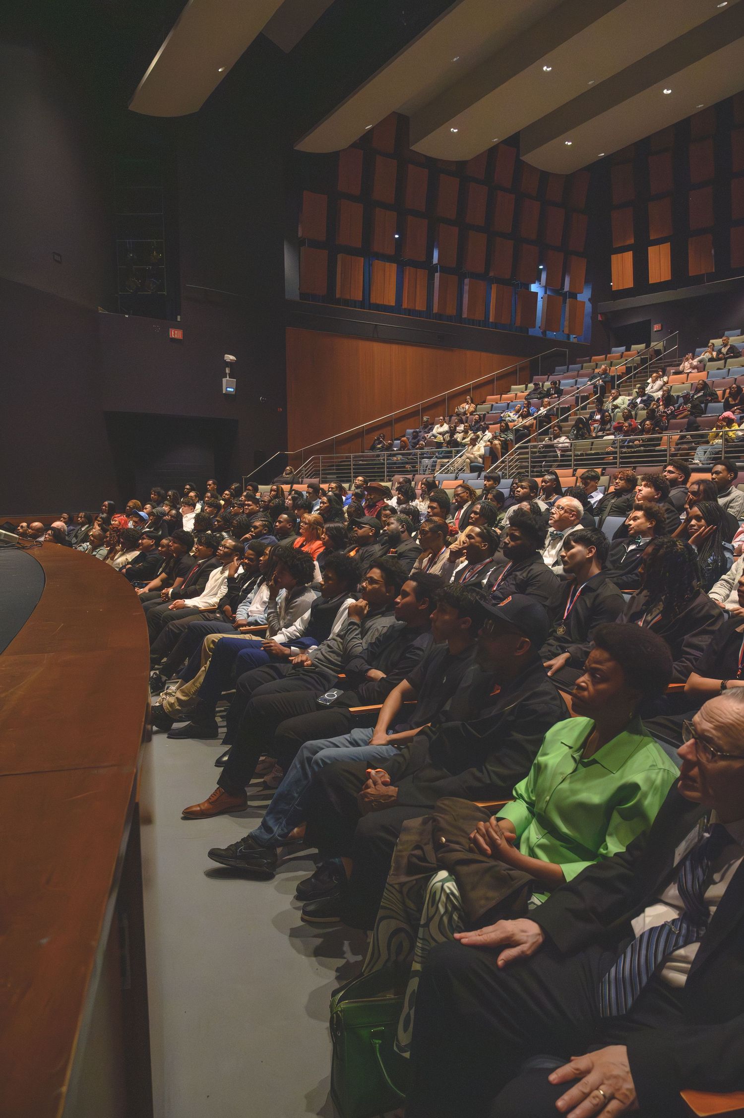 Large audience seated in a modern auditorium during a conference or lecture event, with tiered seating rows fully occupied.