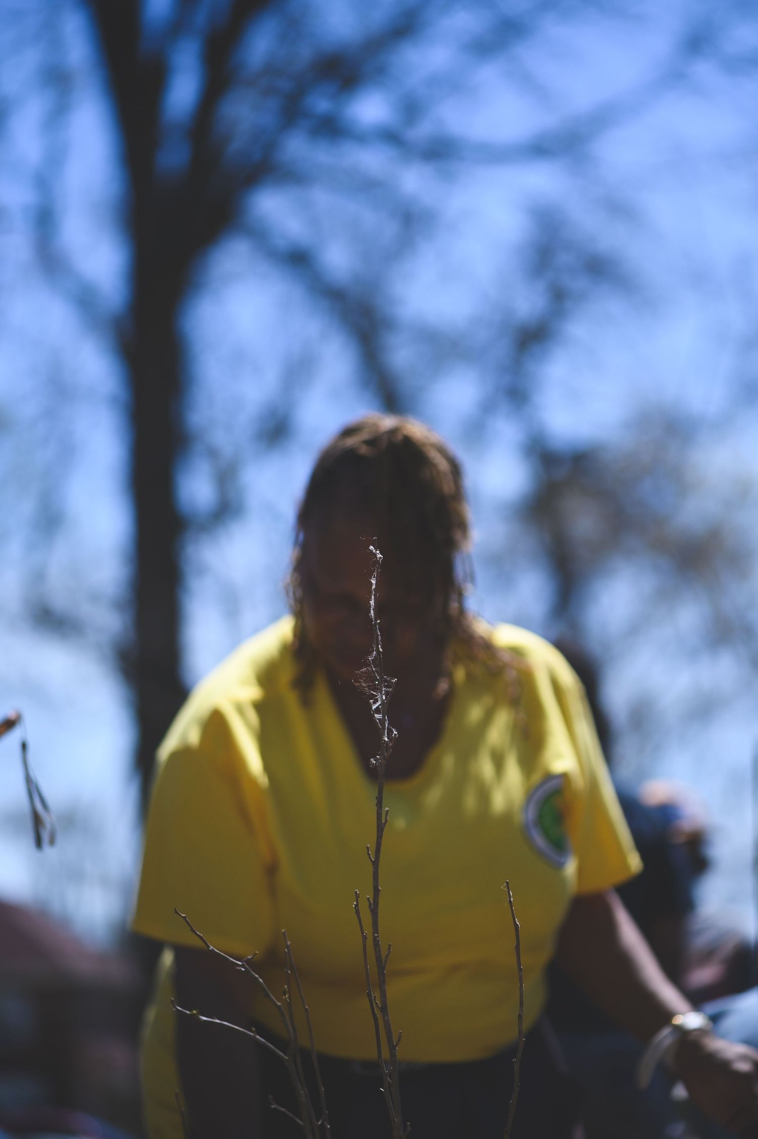 A person wearing a bright yellow t-shirt stands outdoors with tree silhouettes and blue sky in the background.