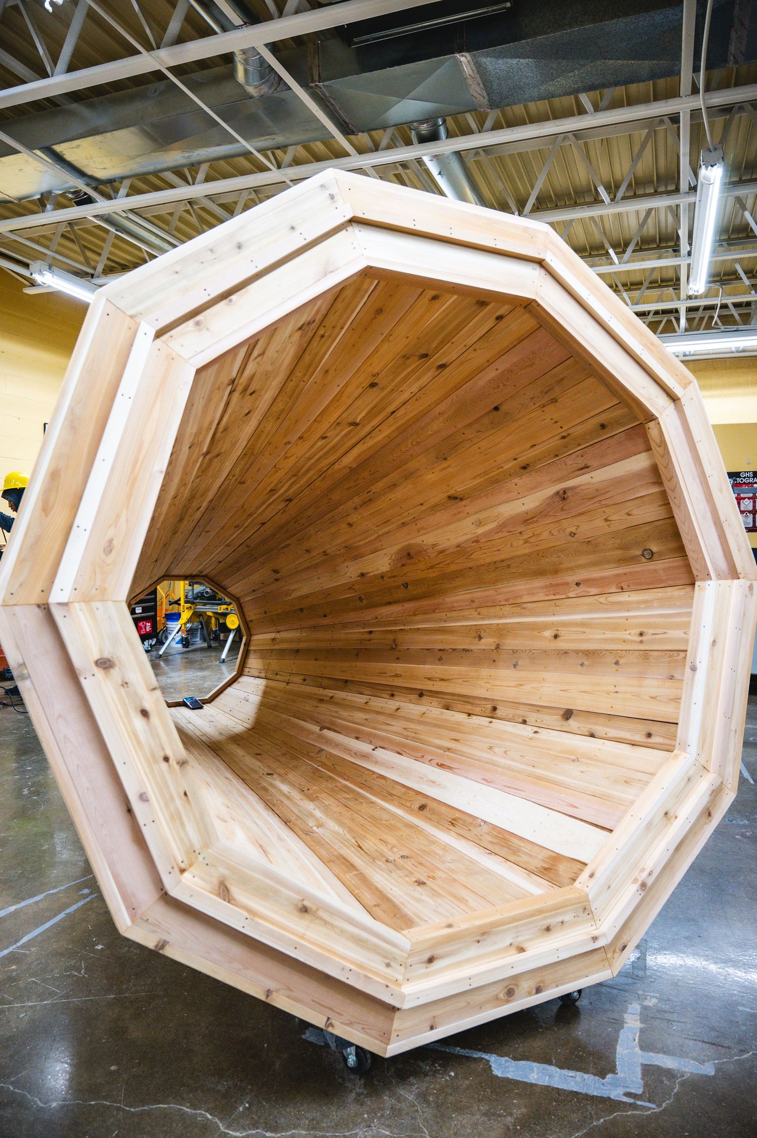 Large handcrafted wooden megaphone structure with octagonal frame and cedar interior, displayed in an industrial workshop space.