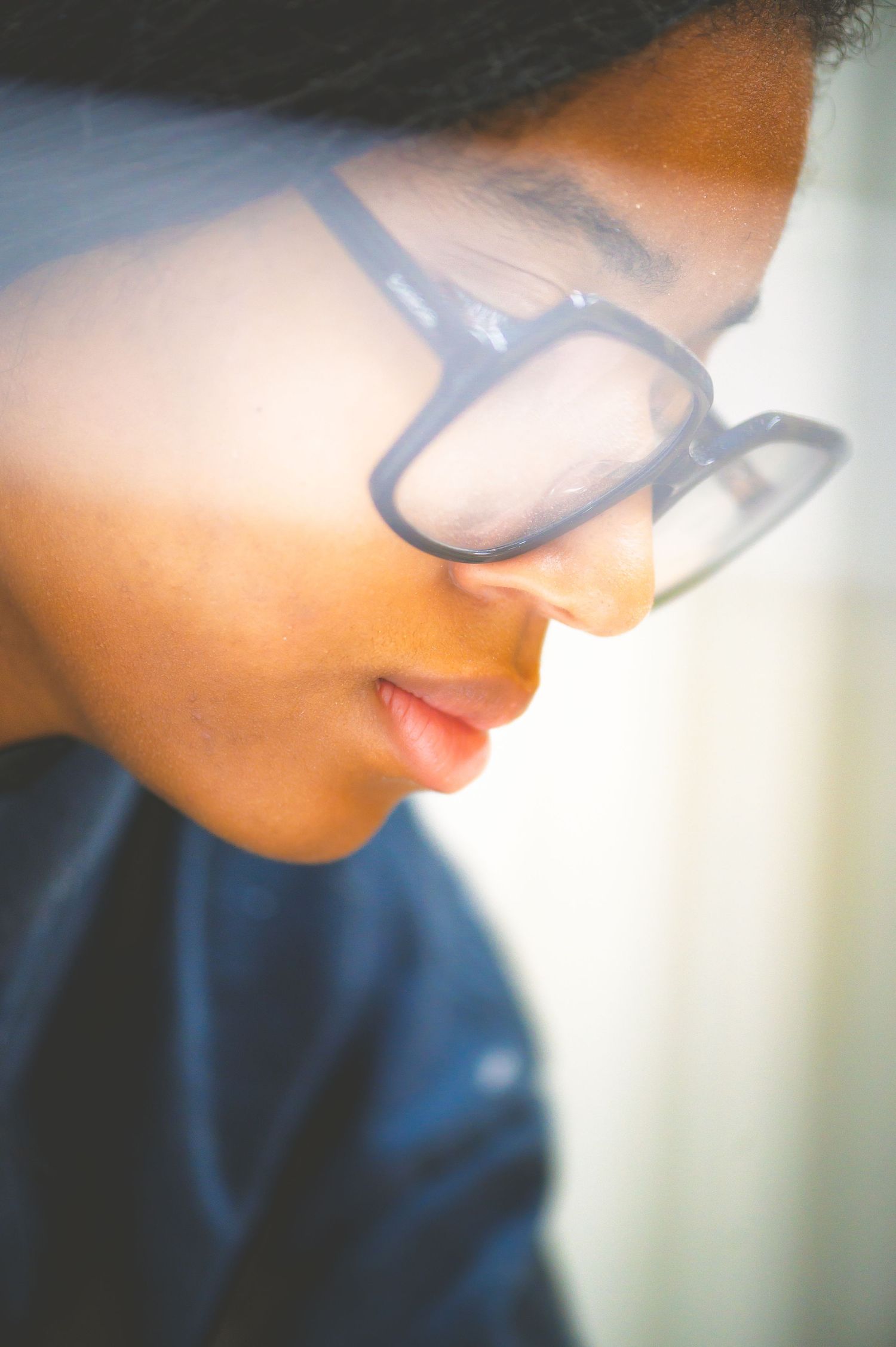 Person wearing glasses shot in artistic soft focus with shallow depth of field and ethereal lighting effect.