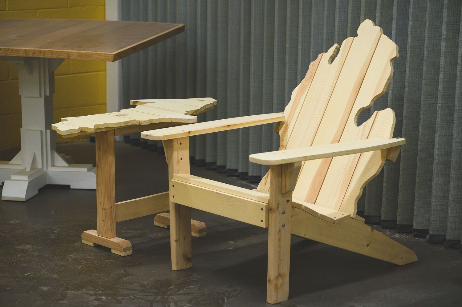 Several unfinished wooden Adirondack chairs are displayed in a row showing different stages of assembly and construction.