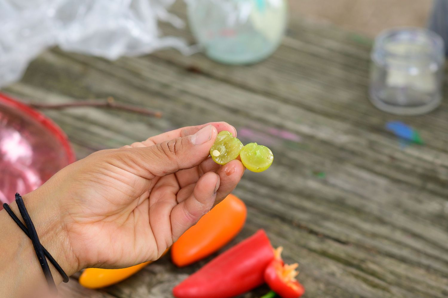 Hand holding small green pepper over wooden table with colorful red and orange peppers in background.