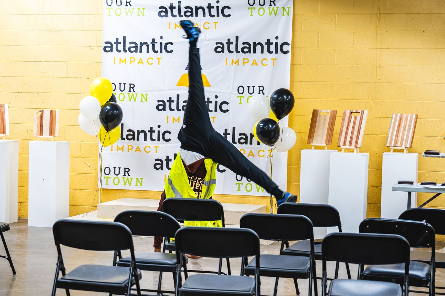 Acrobat performing a handstand at Atlantic Impact event with black and gold balloons and branded backdrop.