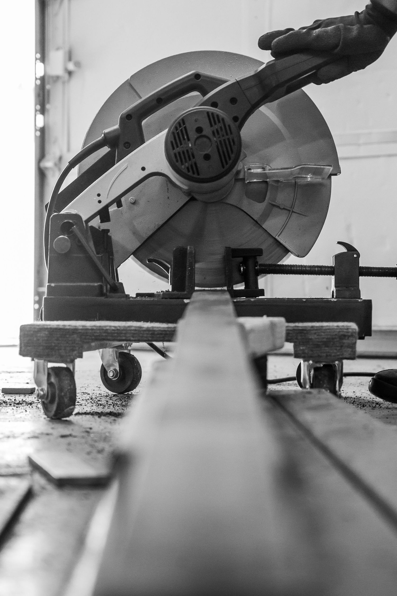 Black and white photo of a metal chop saw cutting steel on a workshop floor.