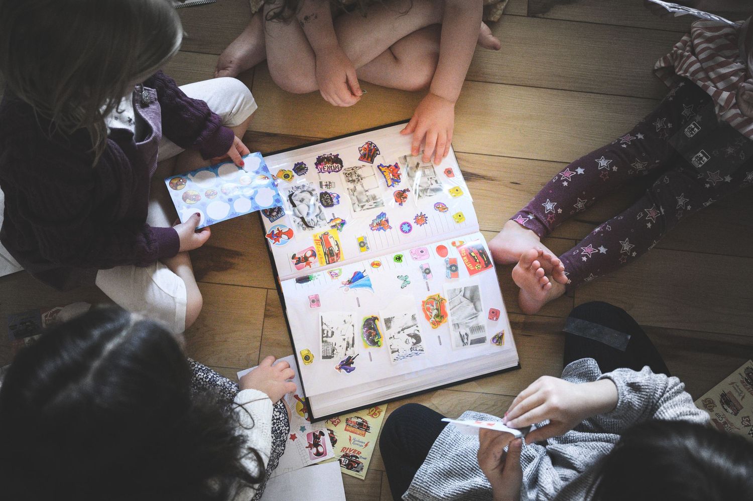 Children sitting on wooden floor playing a colorful board game together, viewed from above.