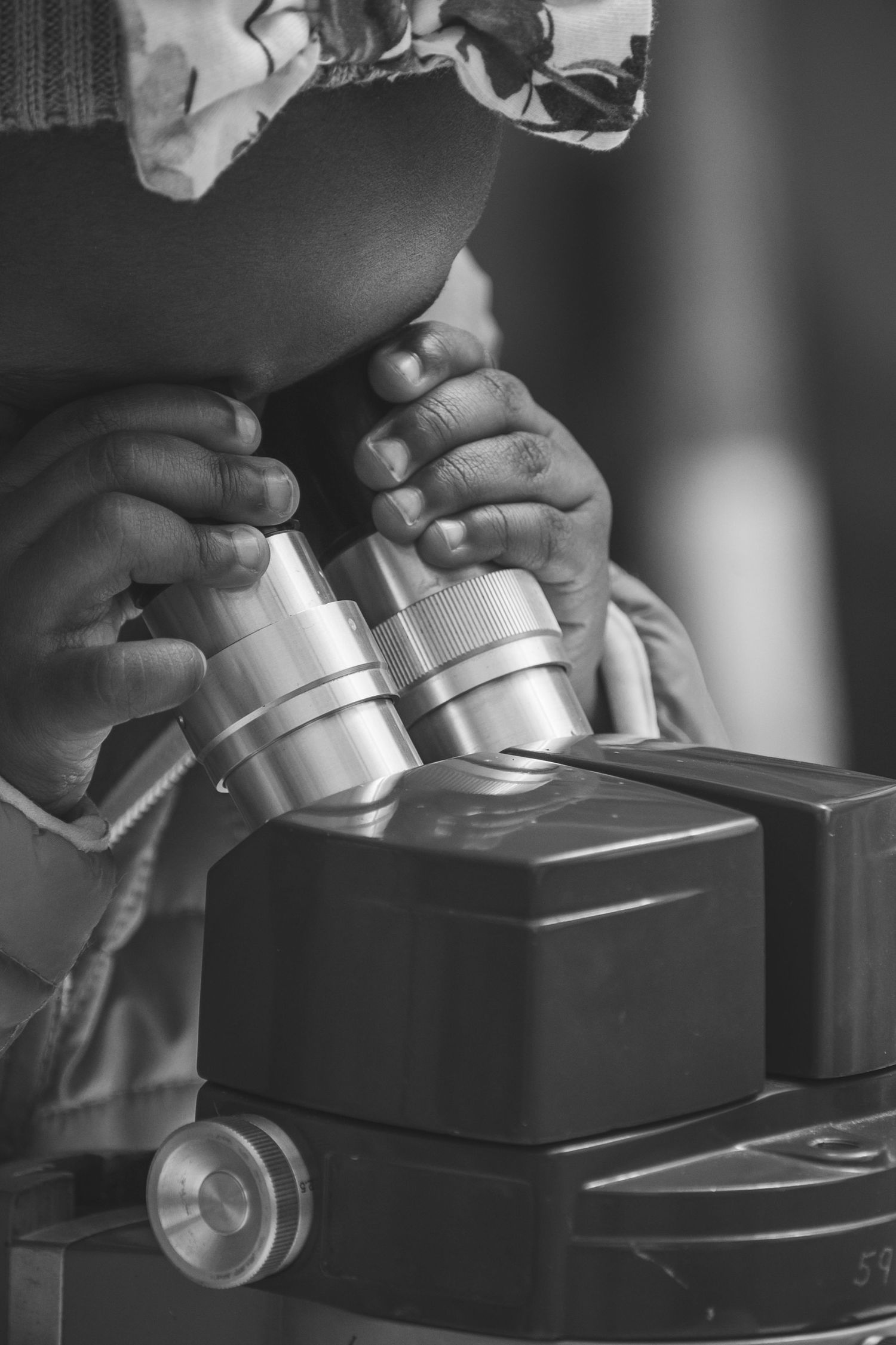 Black and white photo of a child's hands adjusting a microscope eyepiece in a science lab setting.