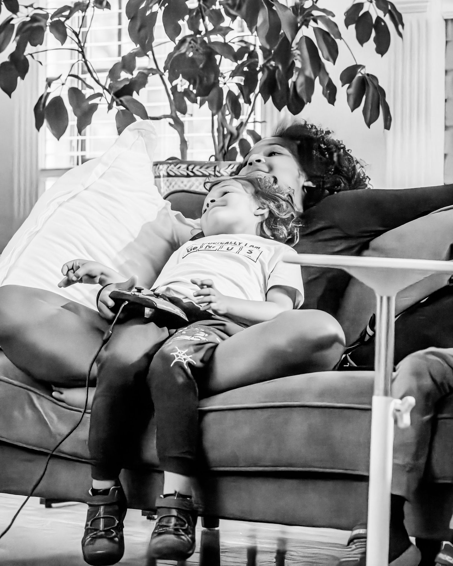 Black and white photo of a parent and child relaxing on a couch, child holding a game controller.