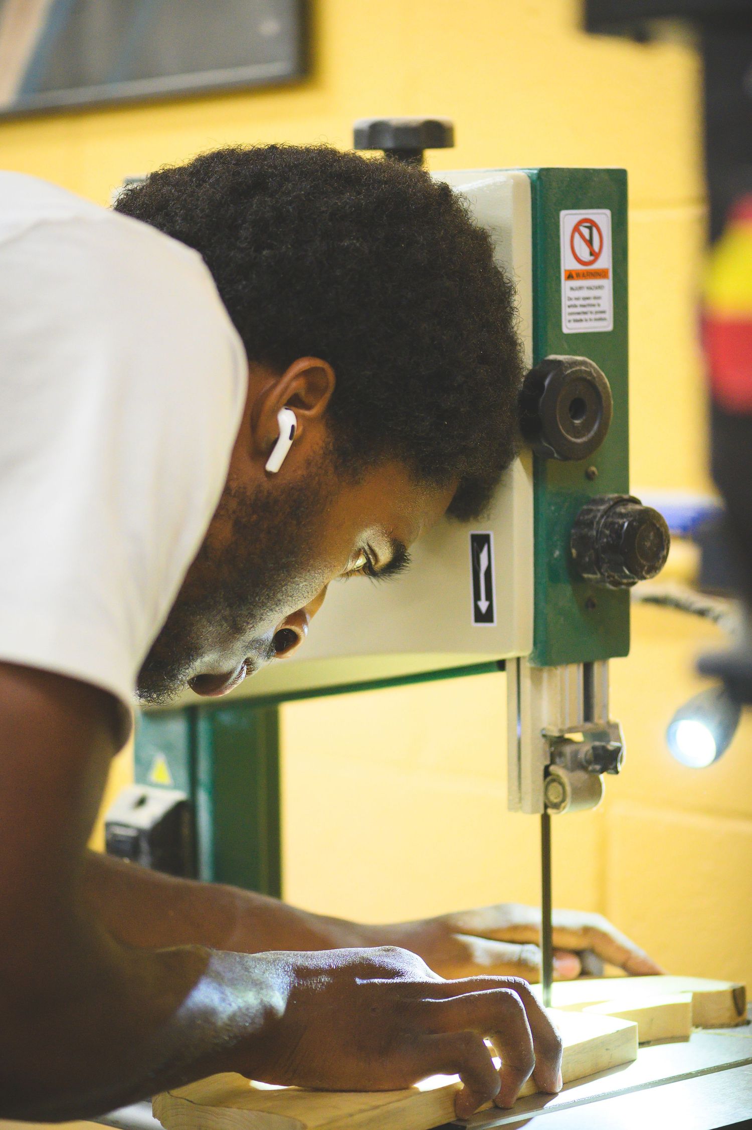 A student uses precision machinery in a vocational training workshop with yellow walls and industrial equipment.