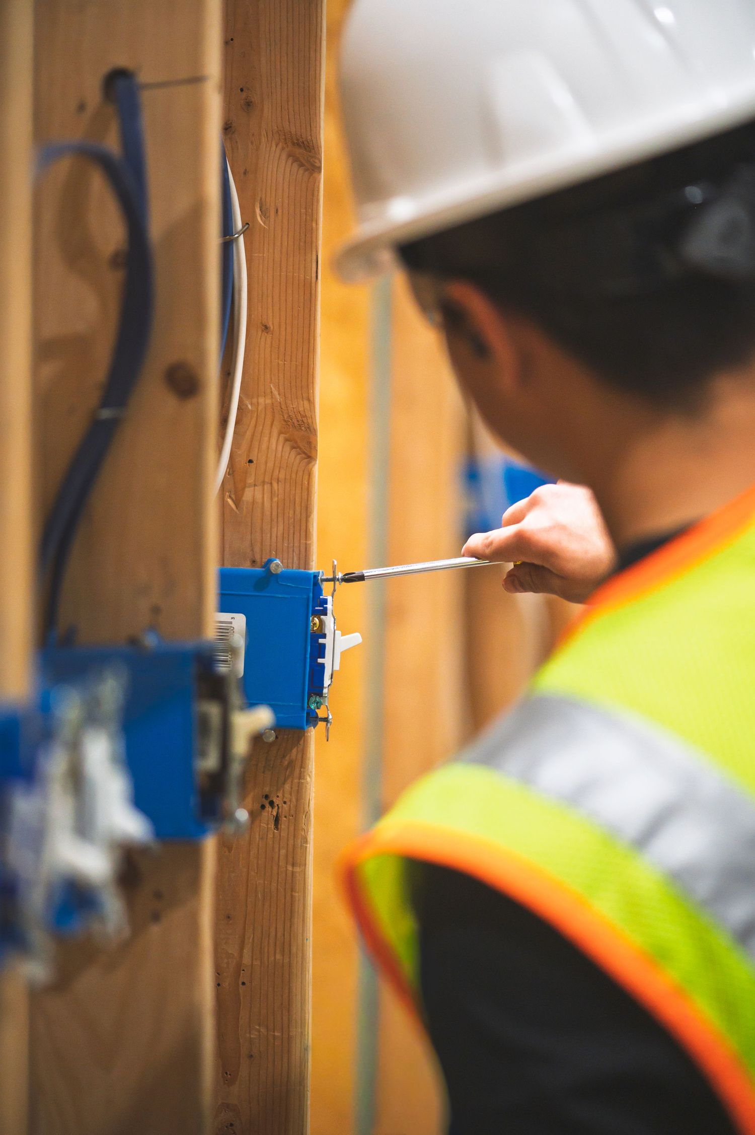 Electrician in safety vest and hard hat using screwdriver on electrical box during construction.