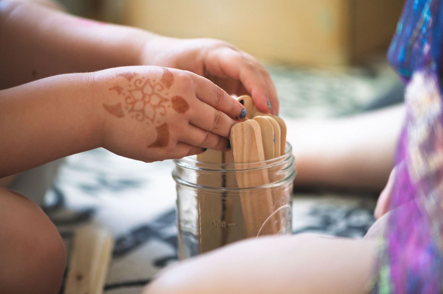Child's hand with henna tattoo placing a wooden stick into a glass jar.