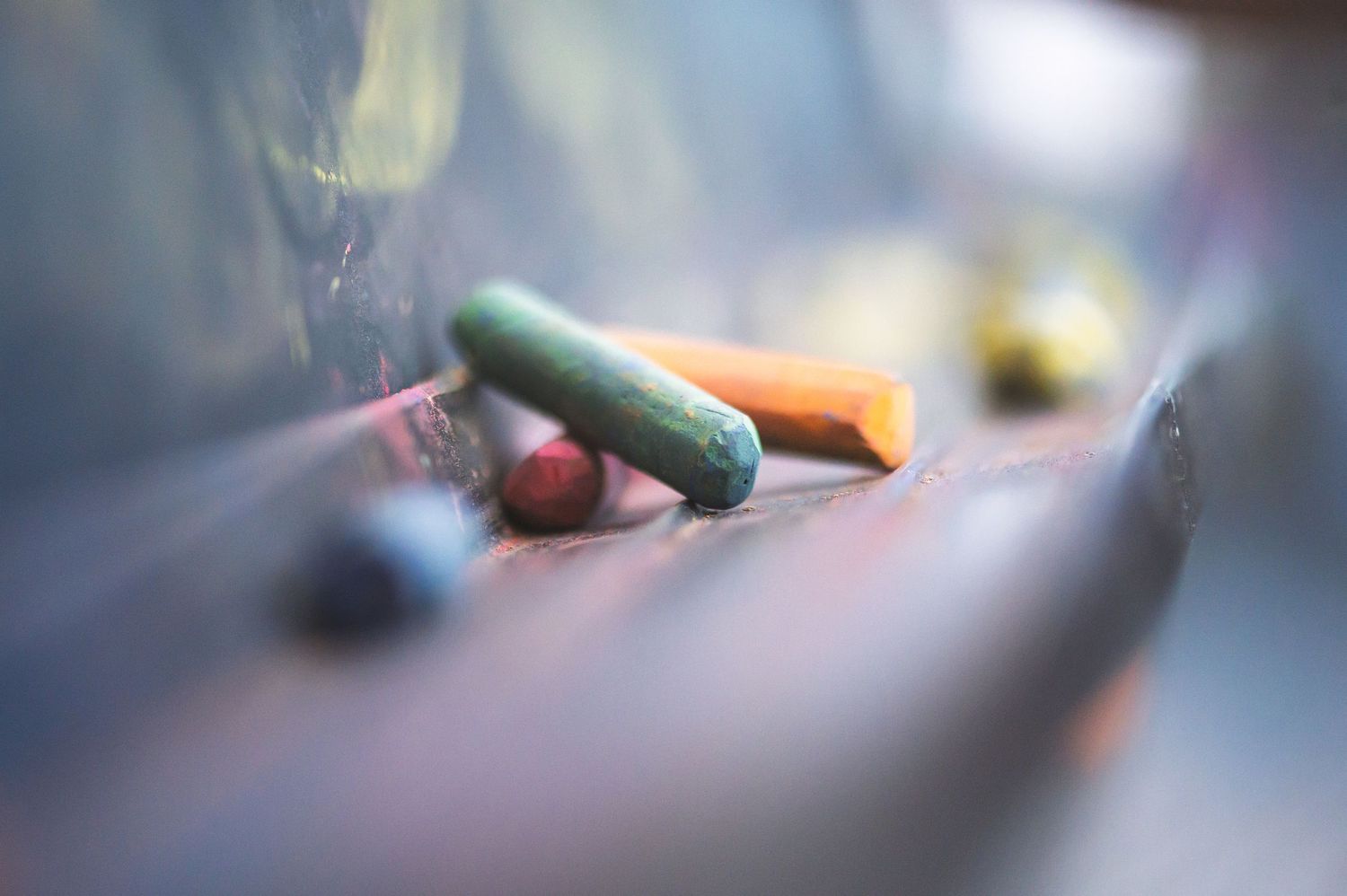 Colorful chalk pieces lie scattered on a blurred dark surface with shallow depth of field.