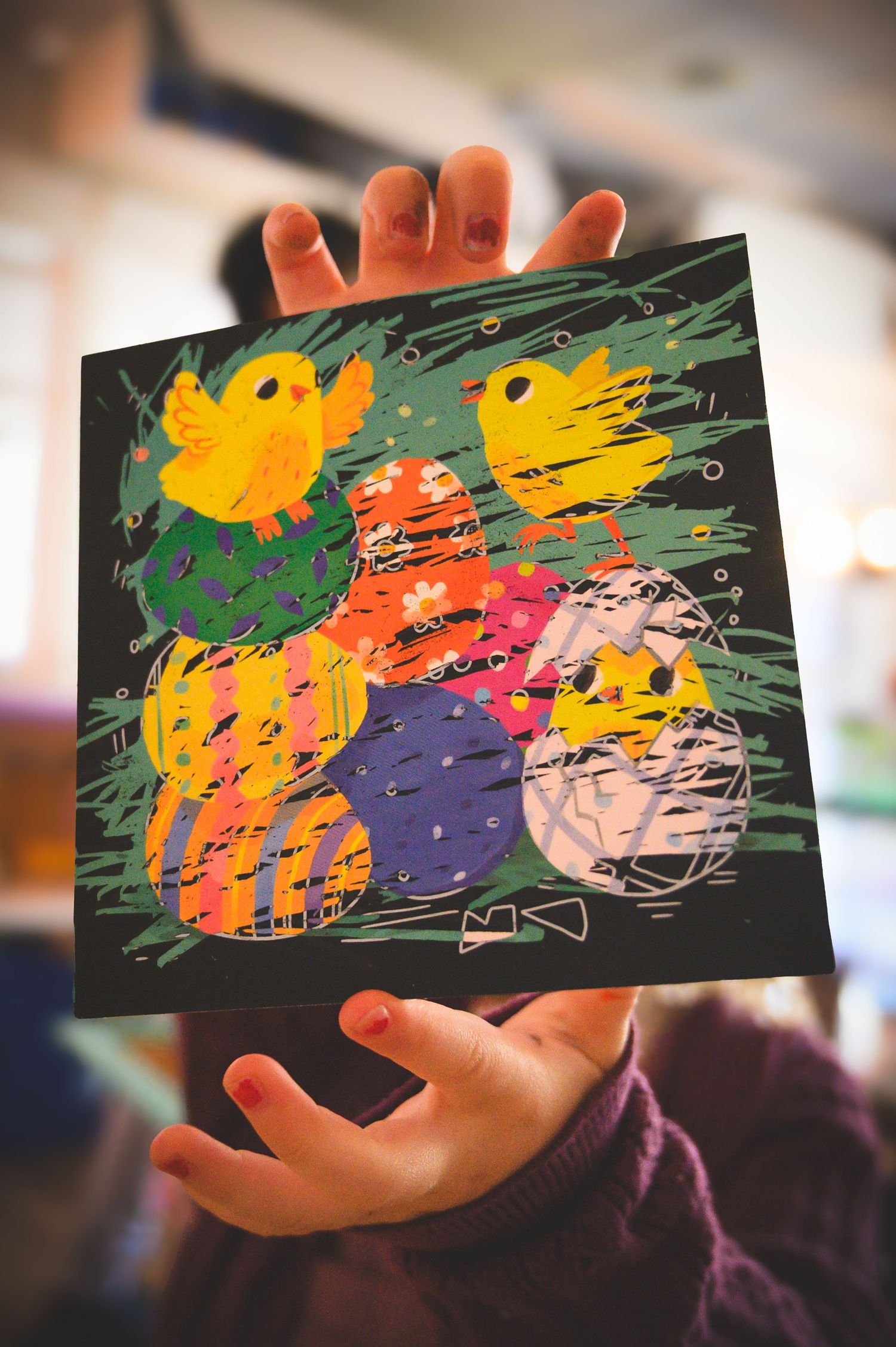 Child holding colorful Easter artwork featuring painted eggs and yellow chicks on black background.