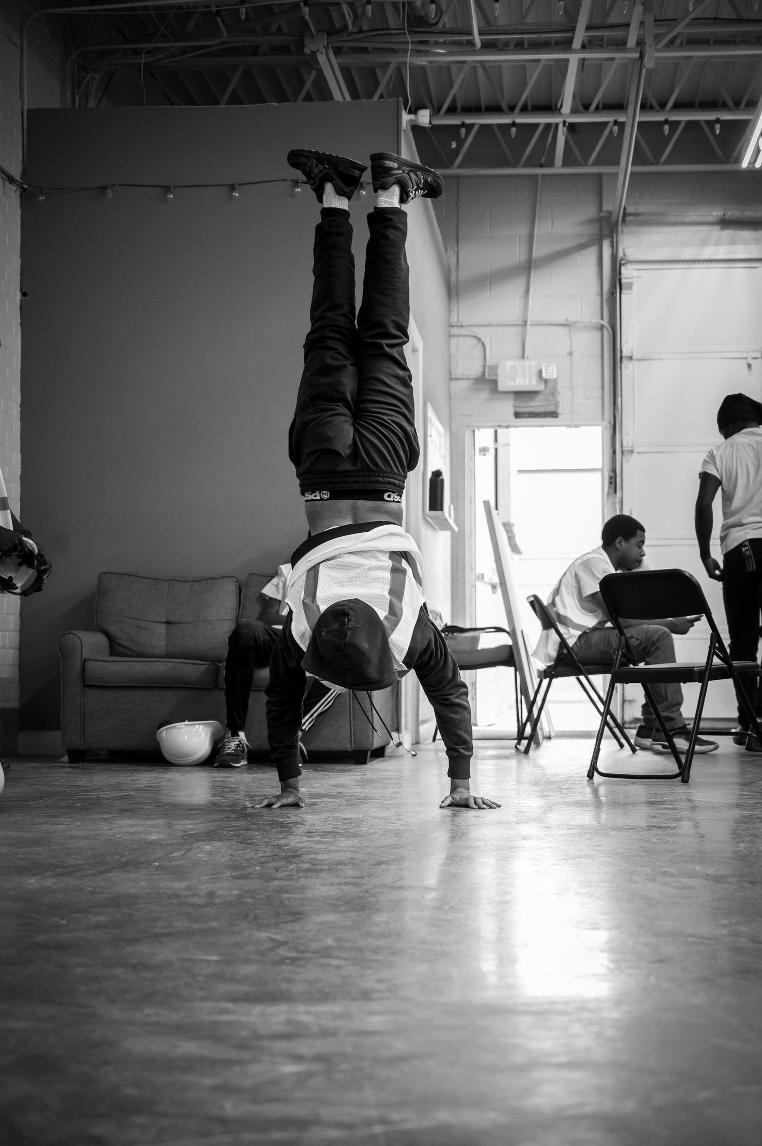 Black and white photo of a person doing a handstand in an indoor space with chairs and a sofa nearby.