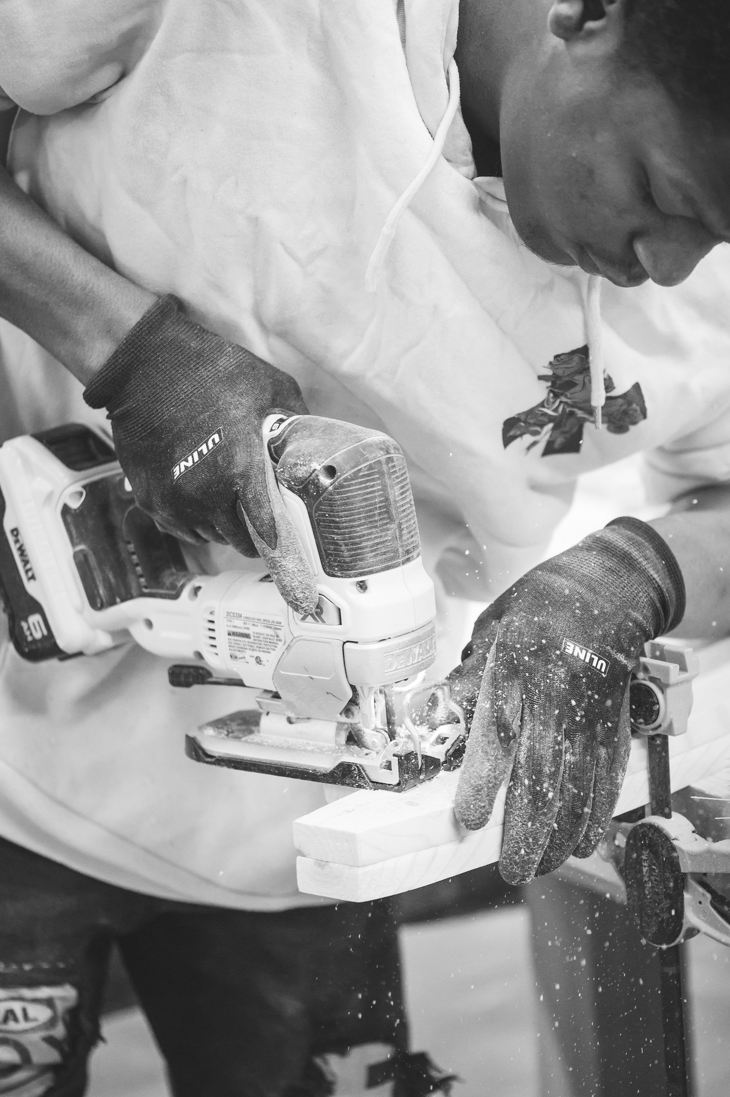 Close-up black and white shot of hands using a power tool on woodwork while wearing protective gloves.