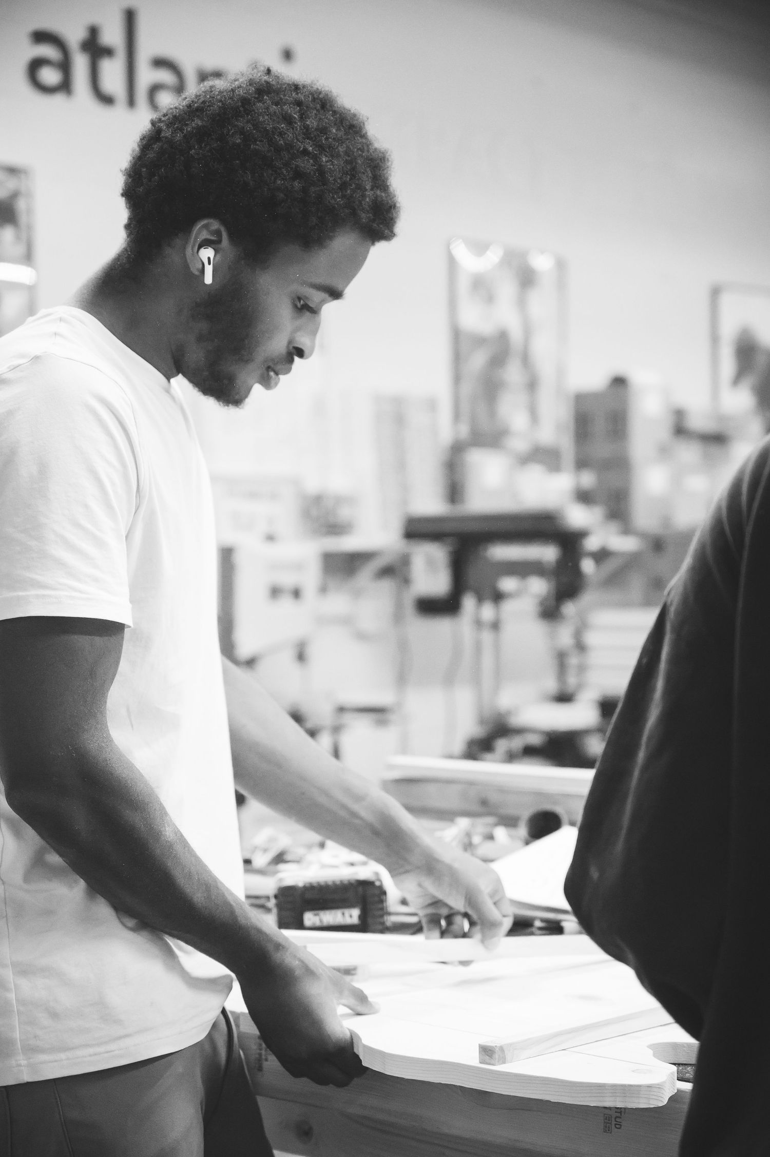 A worker in a white t-shirt carefully reviews and arranges documents while working at a desk in a woodworking setting